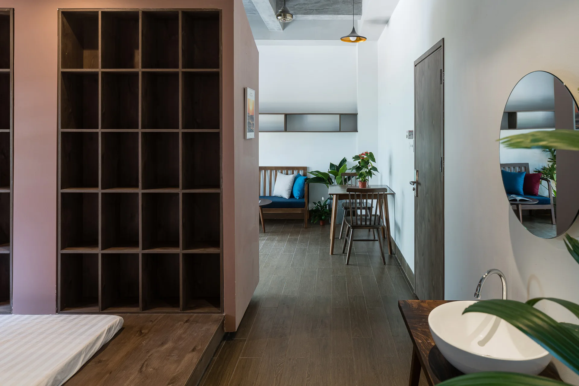 A modern apartment interior features a mauve partition with dark wood grid shelving next to a vanity with a white vessel sink.