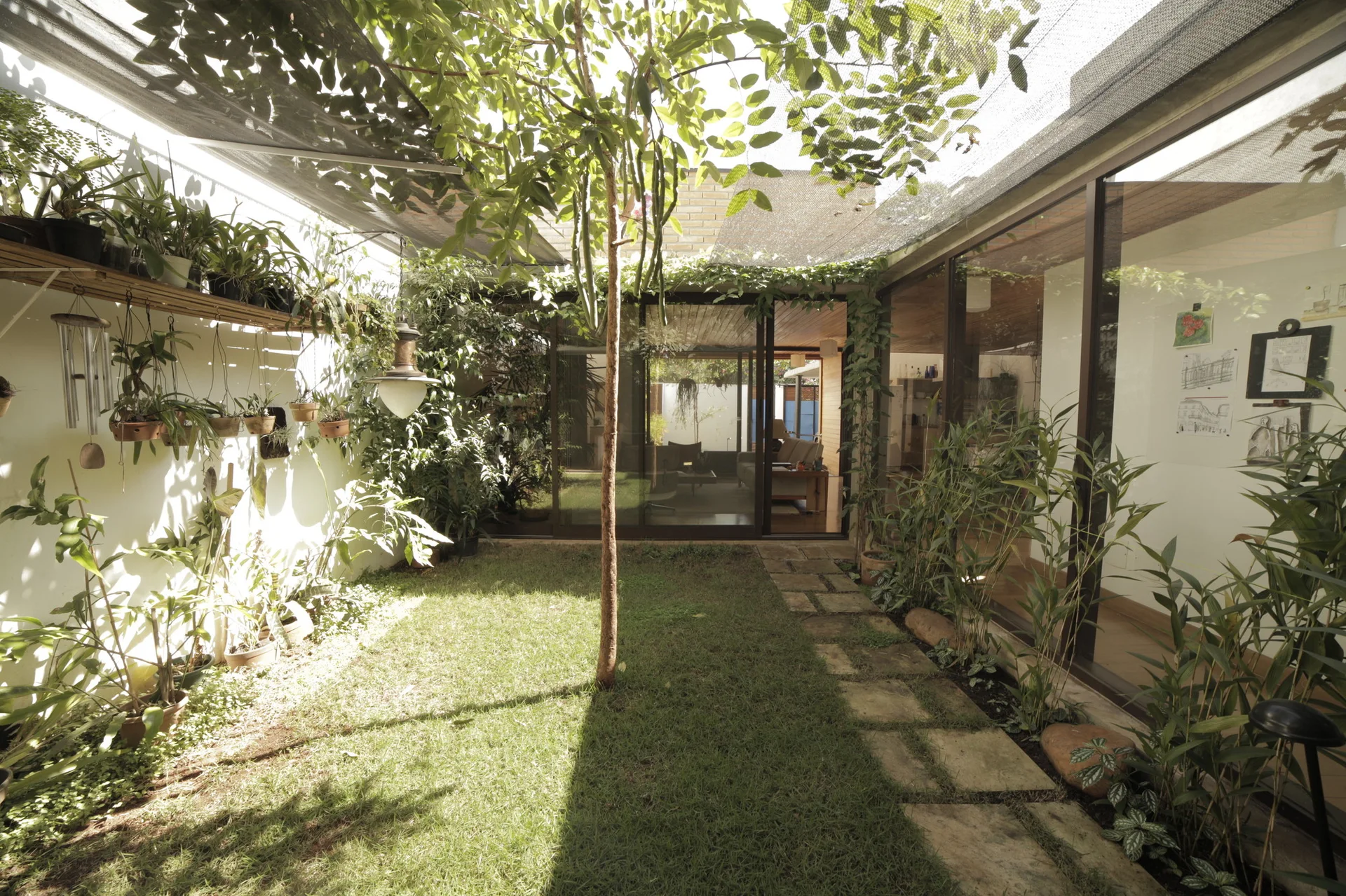 An enclosed residential courtyard features a green lawn, a stone pathway, a central tree, and glass walls looking into the home.