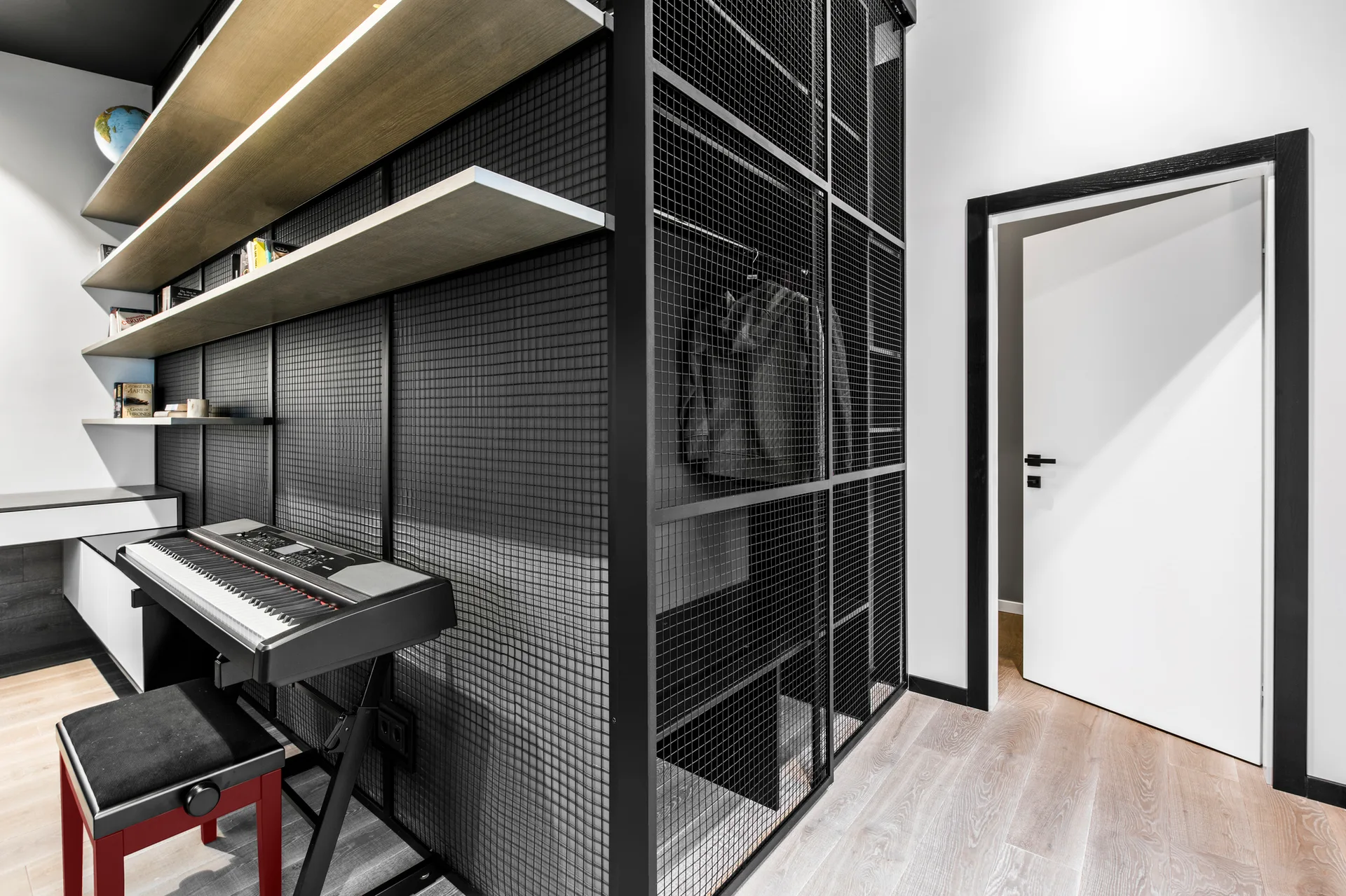 A music room features a black metal mesh wardrobe next to backlit floating wooden shelves, an electronic keyboard, and a white door with black trim.