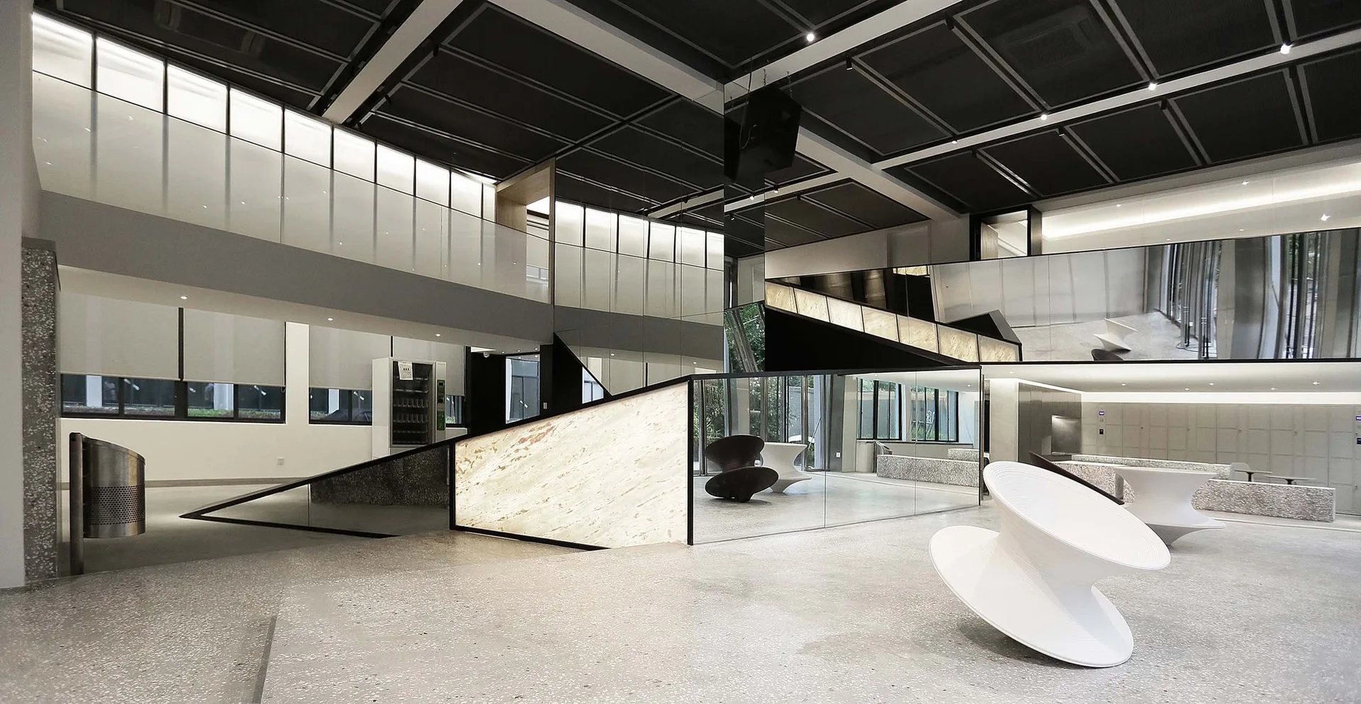 A spacious minimalist lobby features large mirrored walls, a glowing backlit stone reception desk, and white sculptural spiral chairs on a speckled floor.