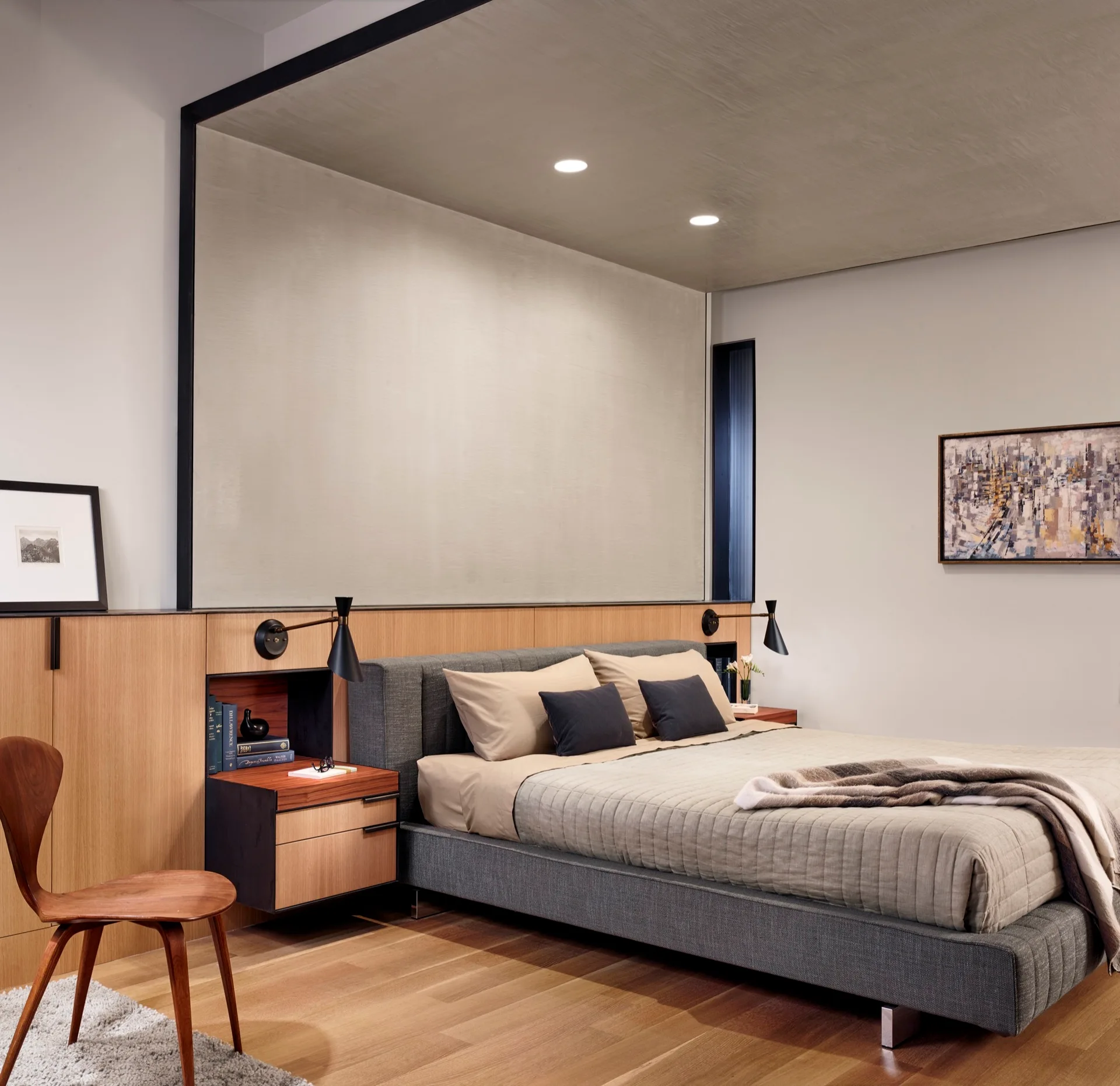 A modern bedroom features a grey upholstered bed set against a custom wood built-in headboard with integrated nightstands and black wall sconces.