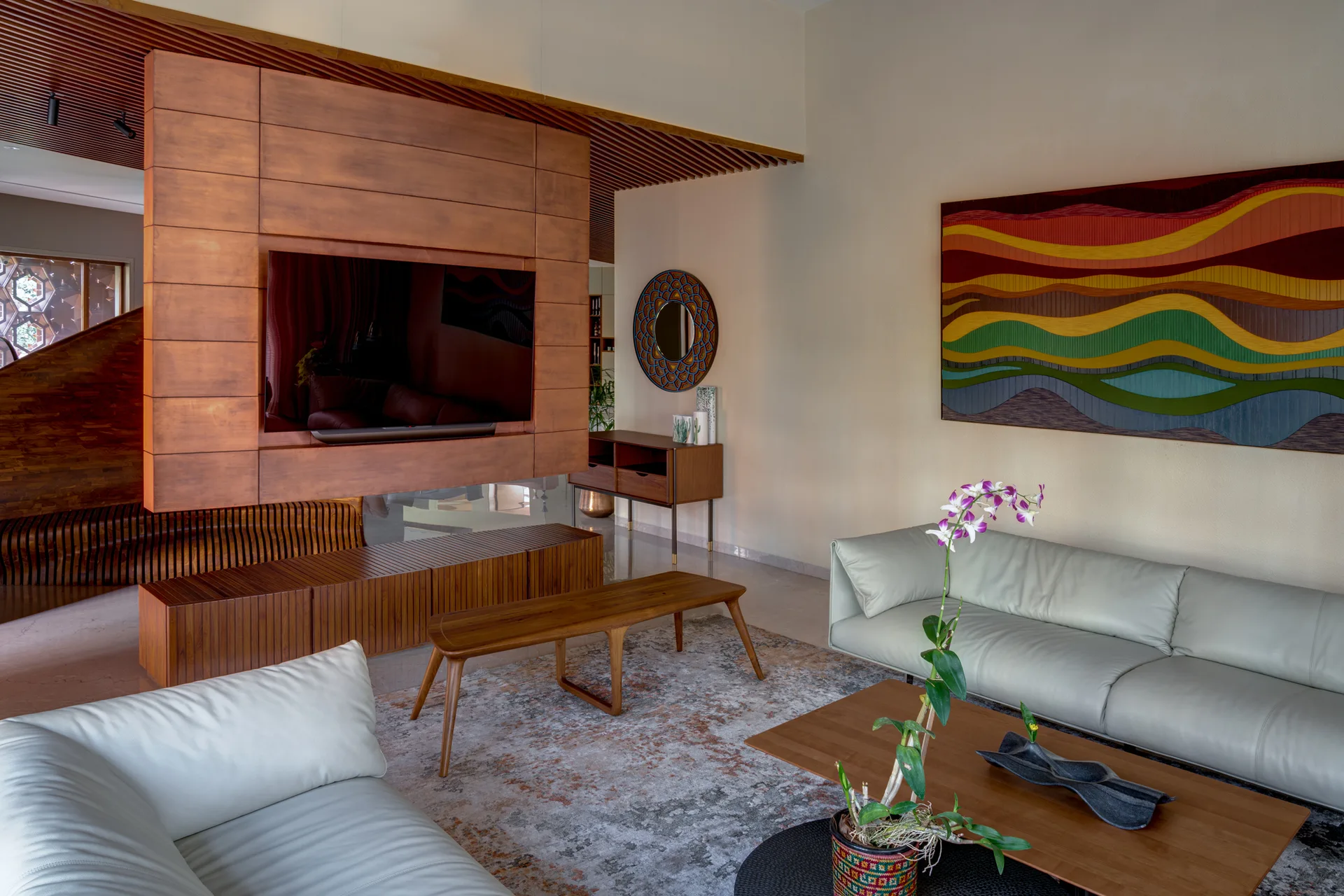 A living room featuring light grey leather sofas, a floating wood media panel, a slatted console, and a colorful abstract painting on the wall.