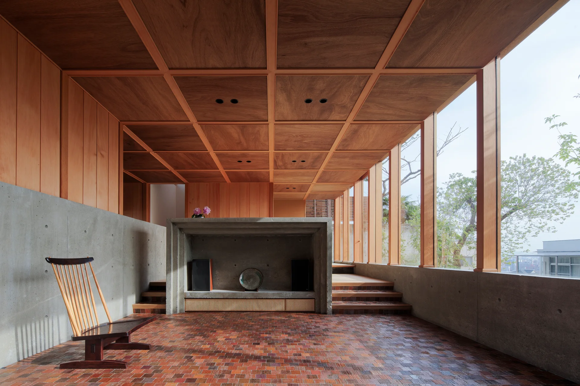 A minimalist room features a grid-patterned wooden ceiling, raw concrete walls, a tiled floor, and a concrete hearth.