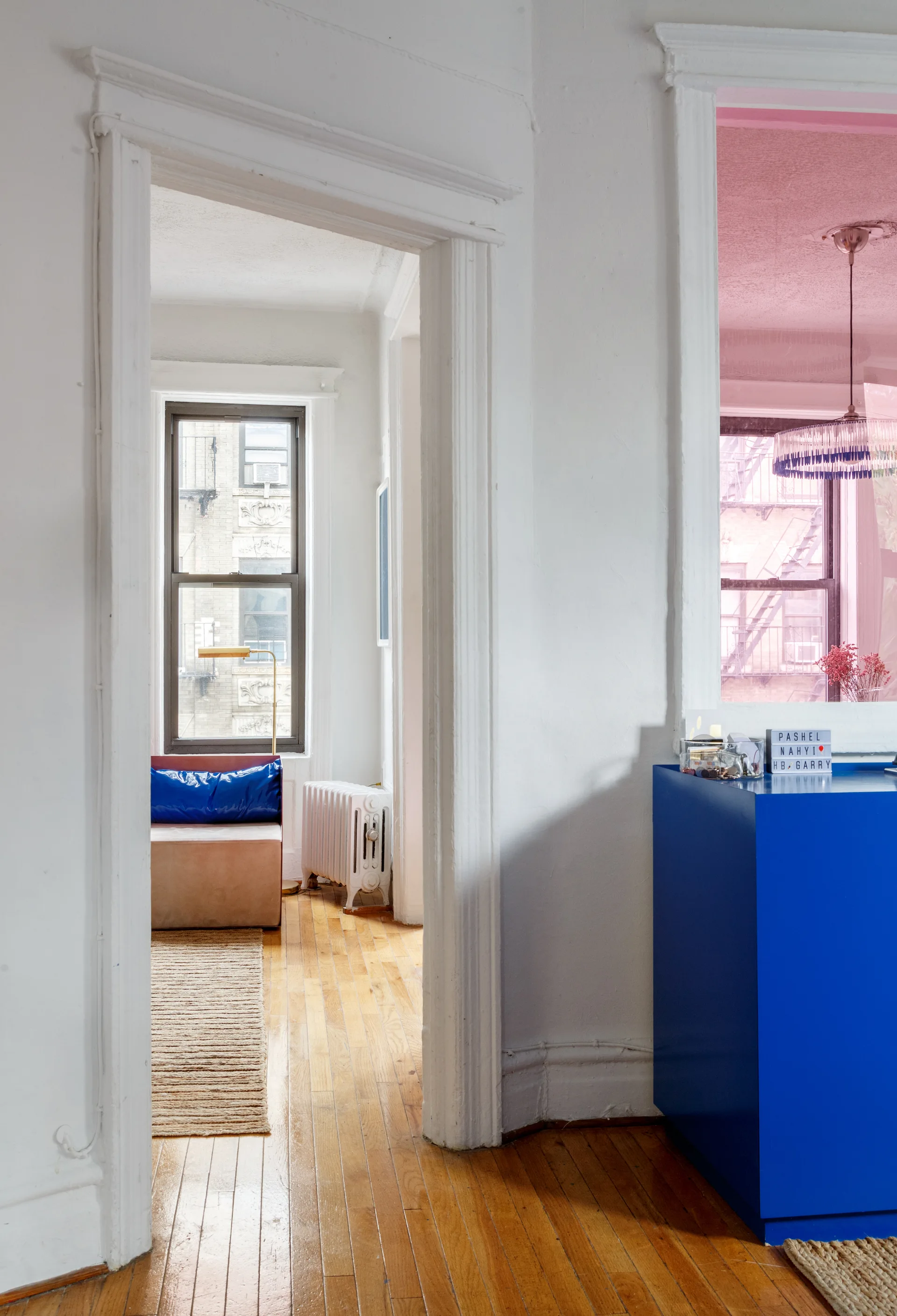 A view through a white door casing shows a glossy cobalt blue cabinet and a living room with hardwood floors and a radiator.