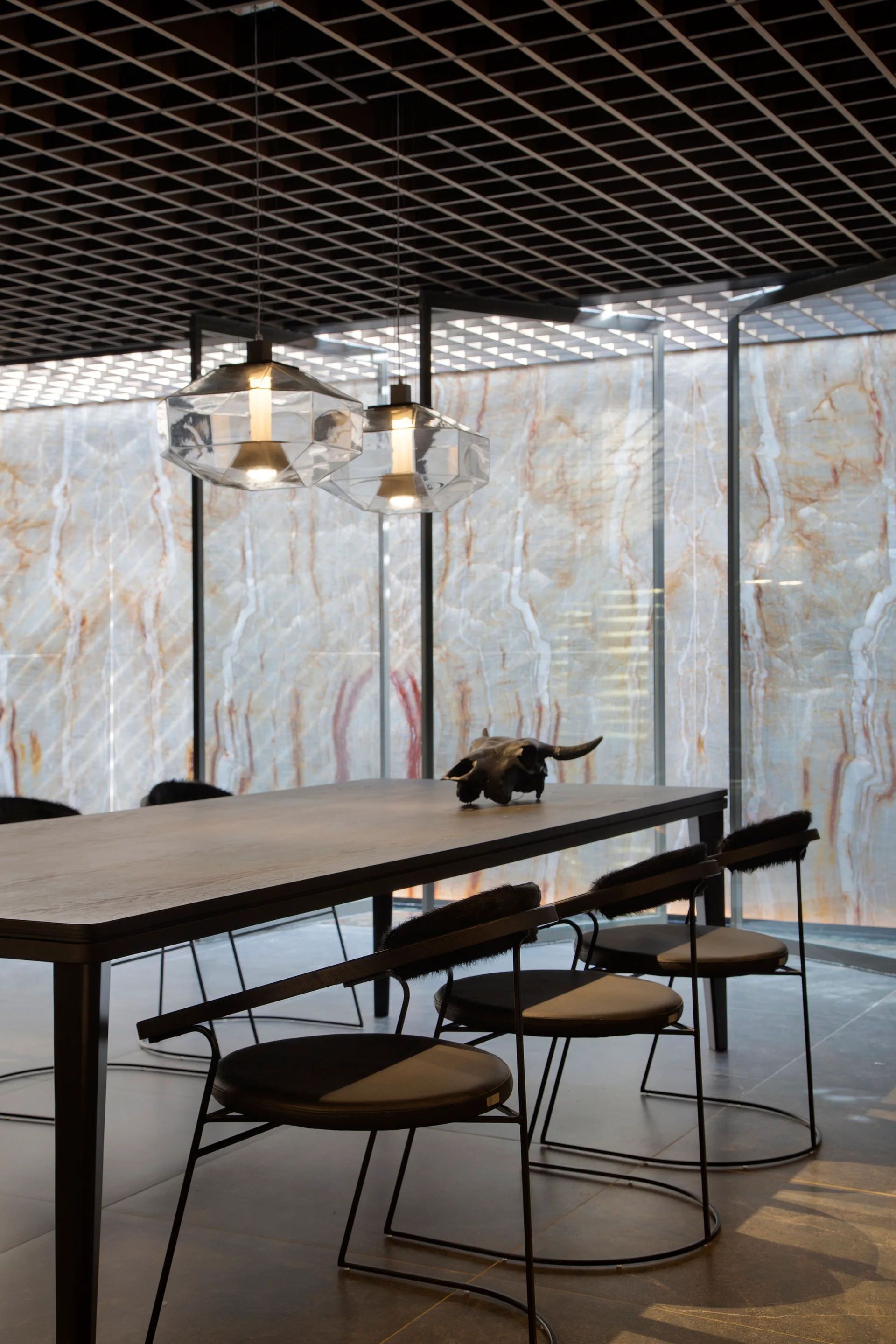 Modern dining room featuring a dark wood table, metal chairs with fur accents, geometric pendant lights, and a backlit veined stone feature wall.
