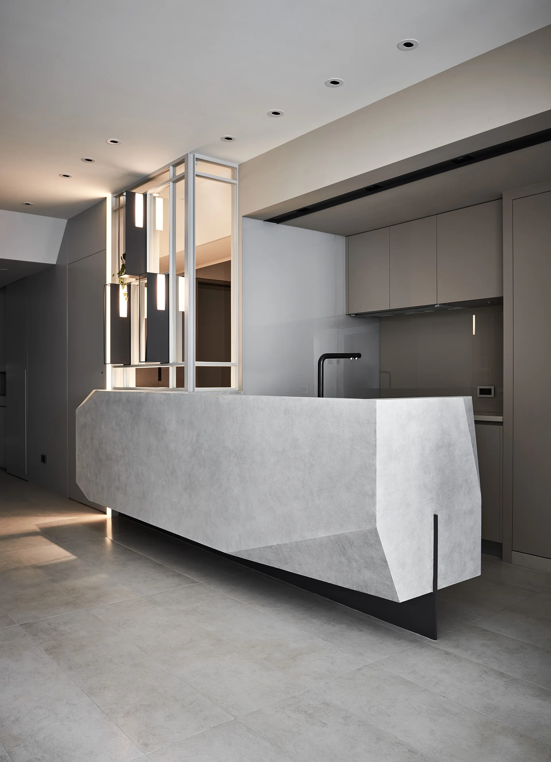 A minimalist grey kitchen features a faceted concrete-look island with a black faucet, set against flat-panel beige cabinets.