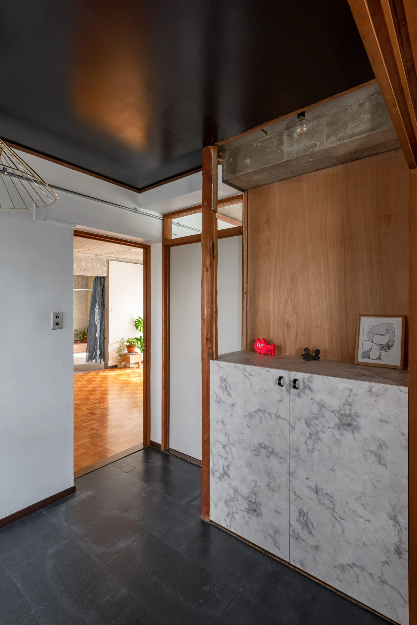 An entryway featuring black tiled floors, a black ceiling, and a low wood cabinet finished with a grey and white marble pattern.