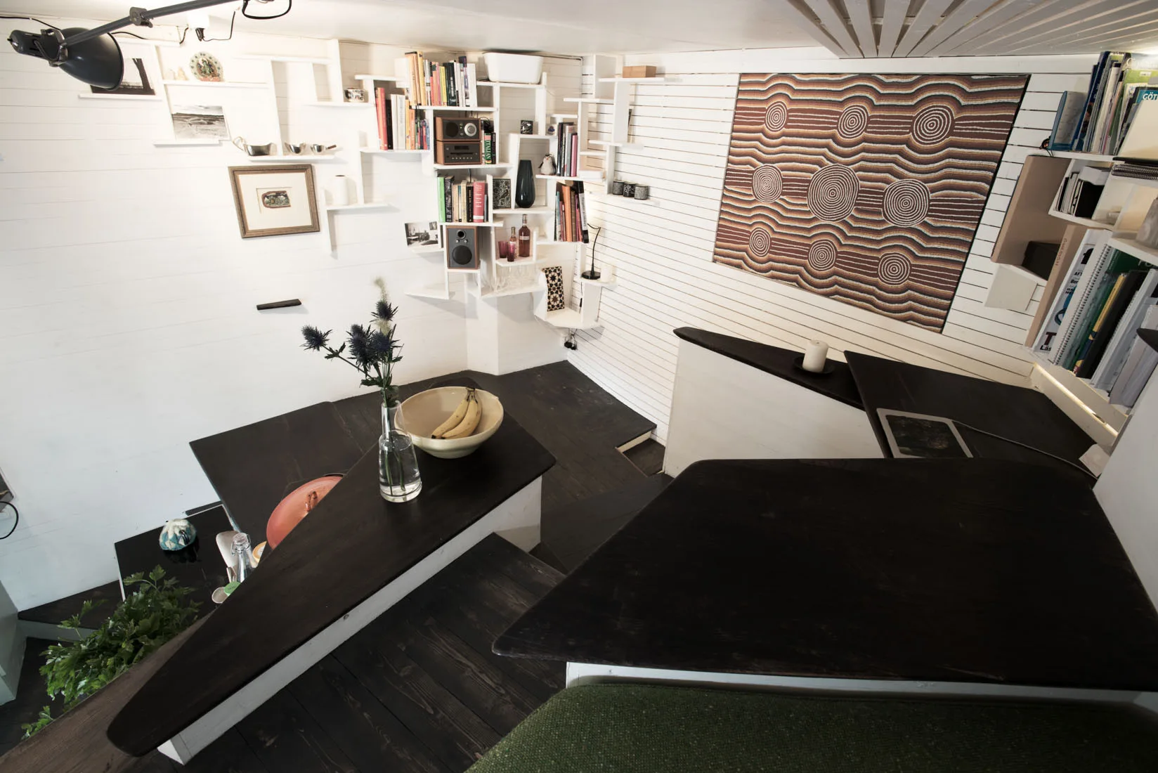 An interior loft space with dark-painted stepped wood platforms, white shiplap walls with custom grid shelving, and patterned textile wall art.
