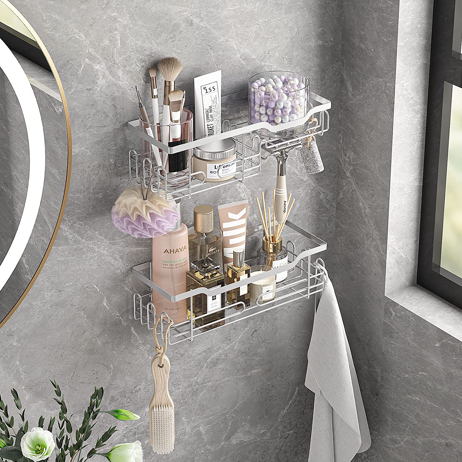 A two-tier metal wire shelf mounted on a gray marble bathroom wall holds various beauty products, makeup brushes, and a hanging white towel.
