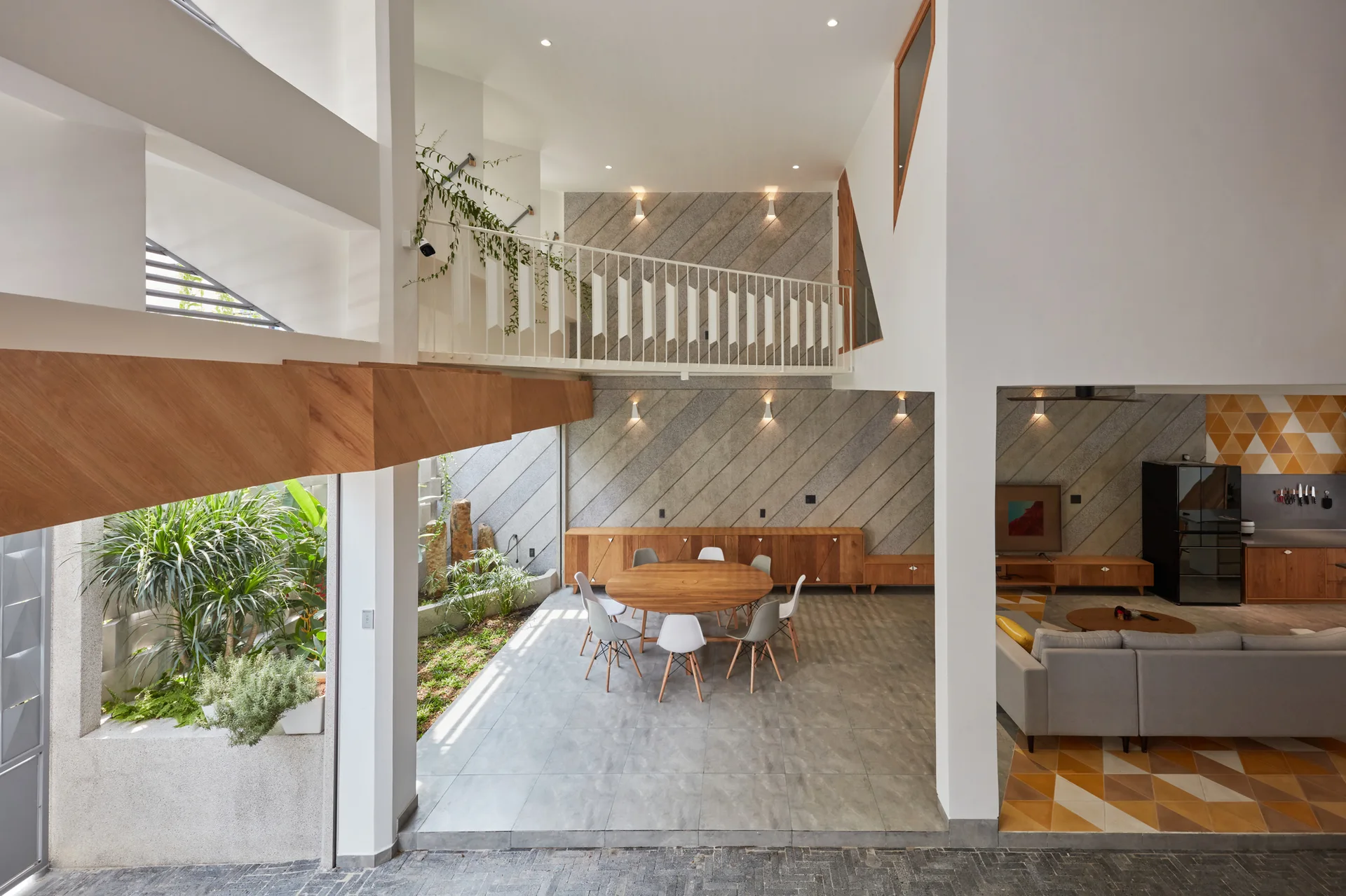 A spacious modern dining area features a round wooden table and chairs, set against a diagonal stone wall next to an indoor courtyard.