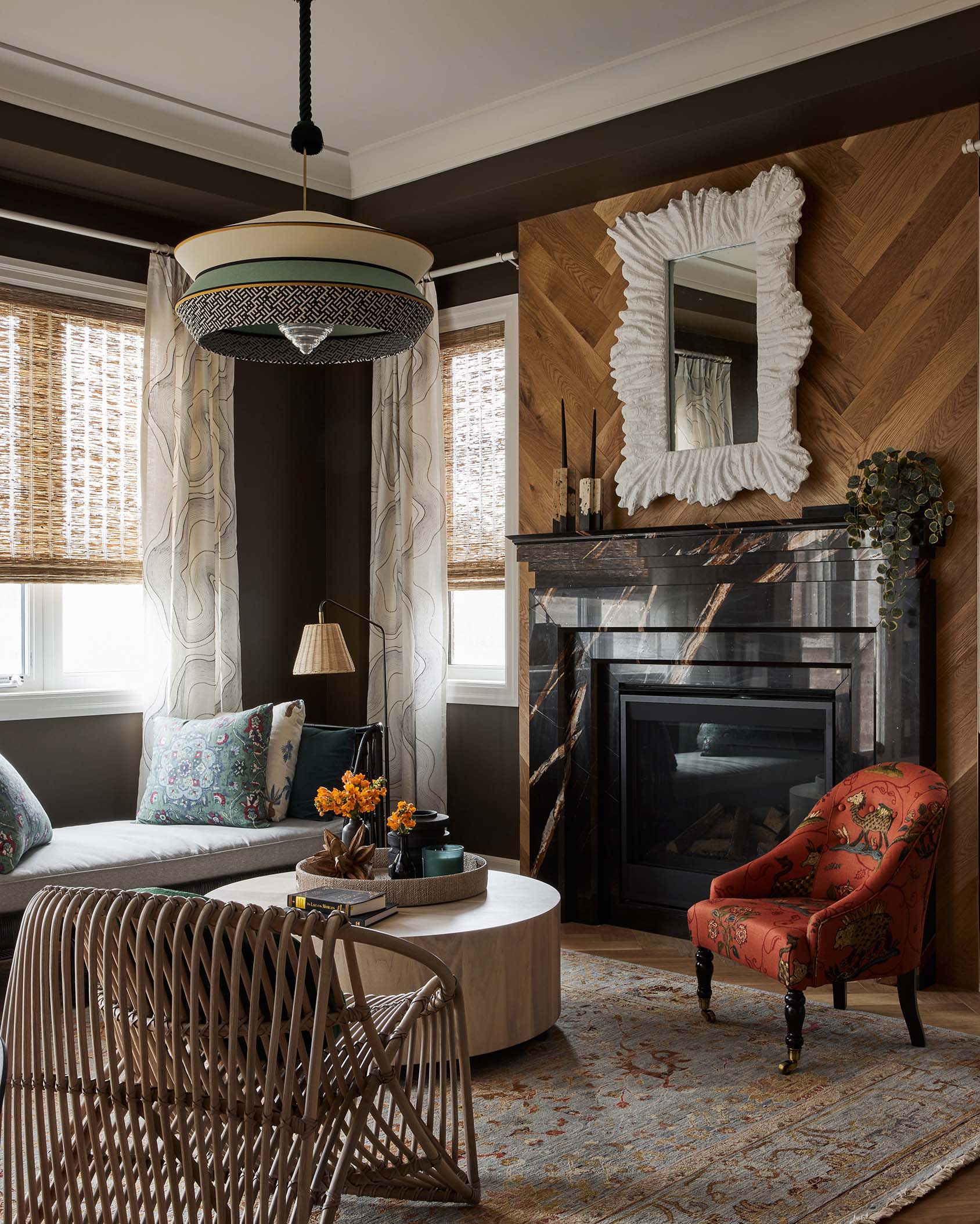 An eclectic living room featuring a black marble fireplace set against a herringbone wood wall with a textured white mirror.