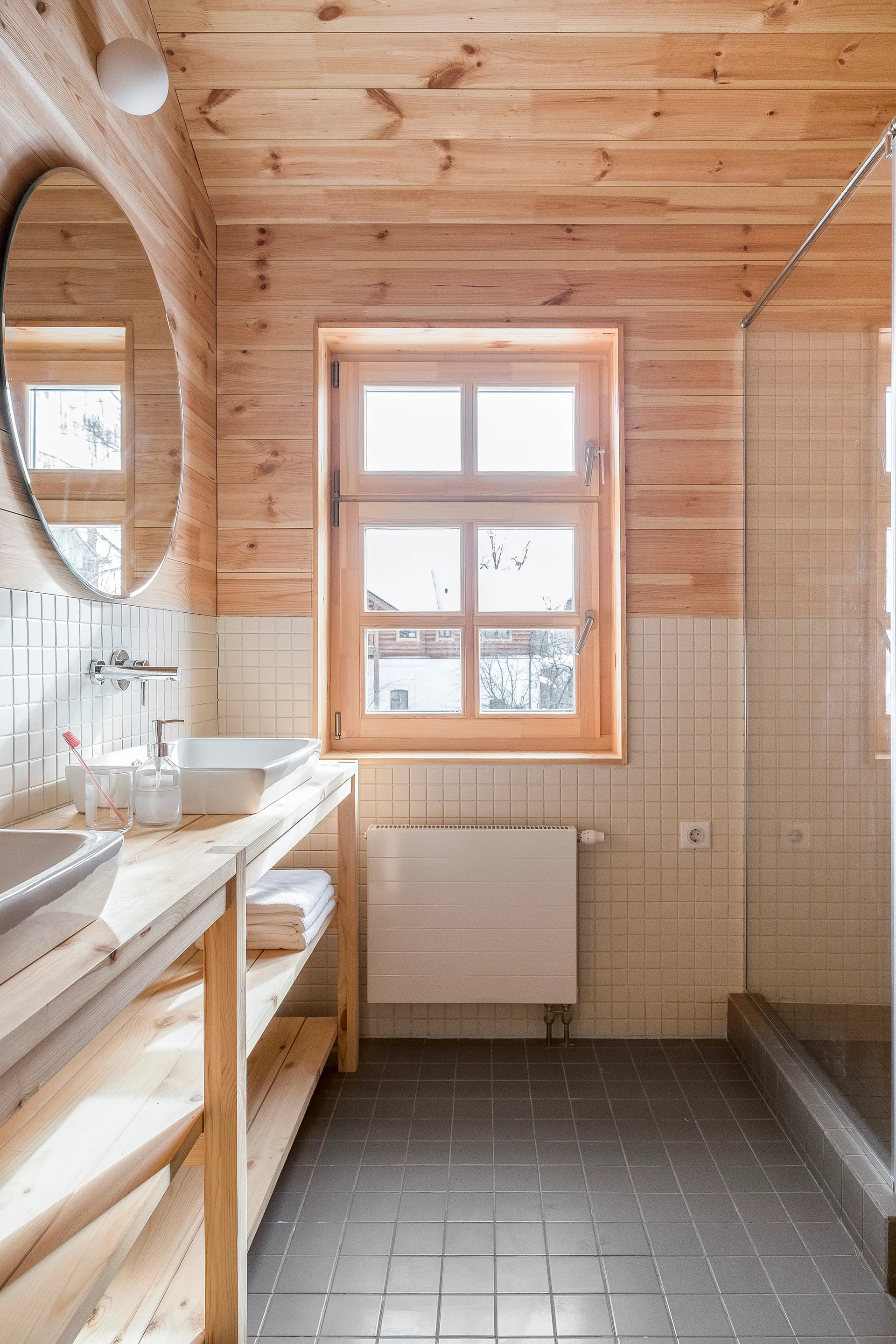 A bathroom featuring knotty pine wall paneling, a white tiled backsplash, a light wood open vanity with a vessel sink, and a grey tile floor.