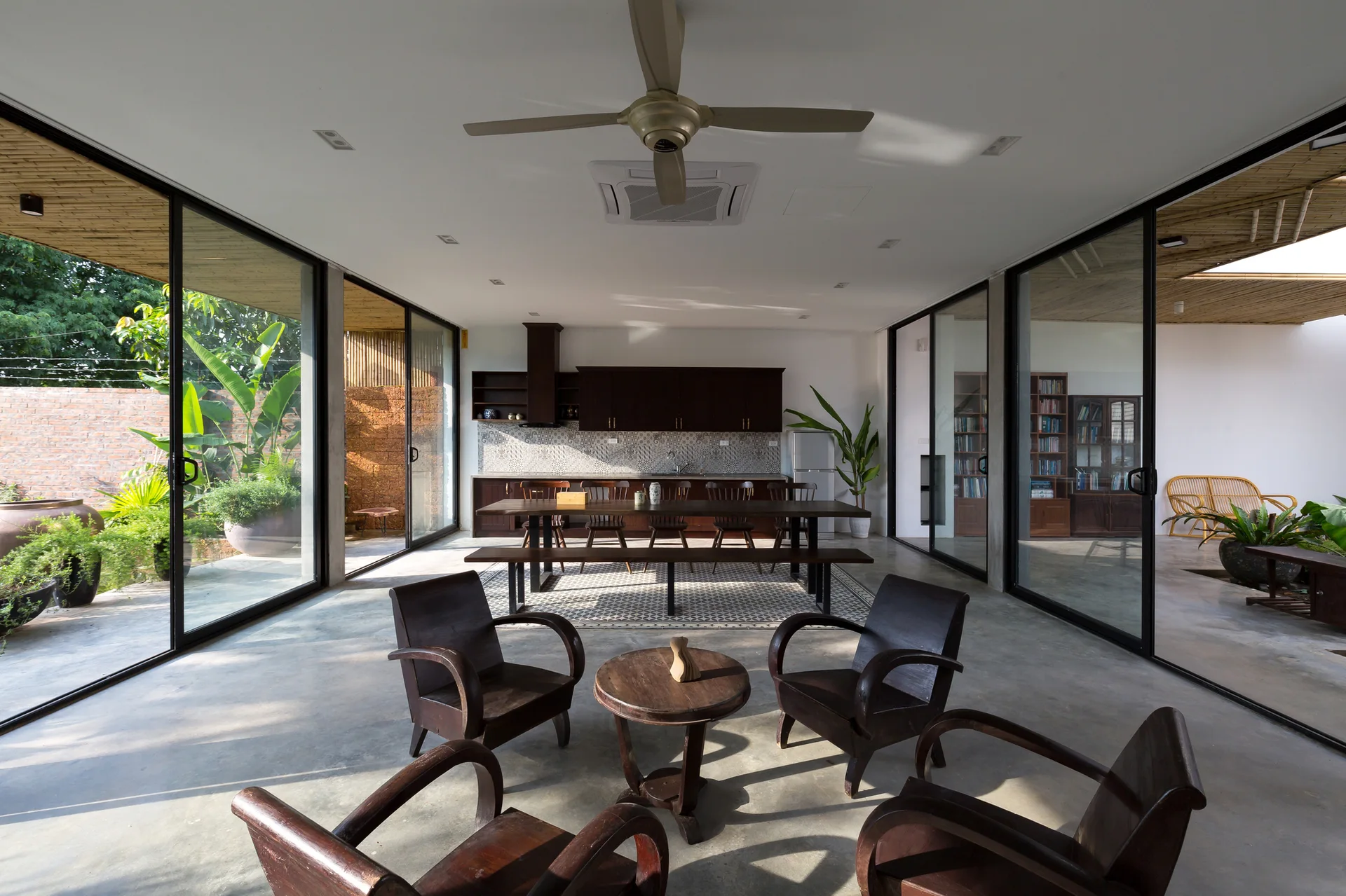 An open-concept living and dining area features polished concrete floors, dark wood furniture, and floor-to-ceiling sliding glass doors on both sides.