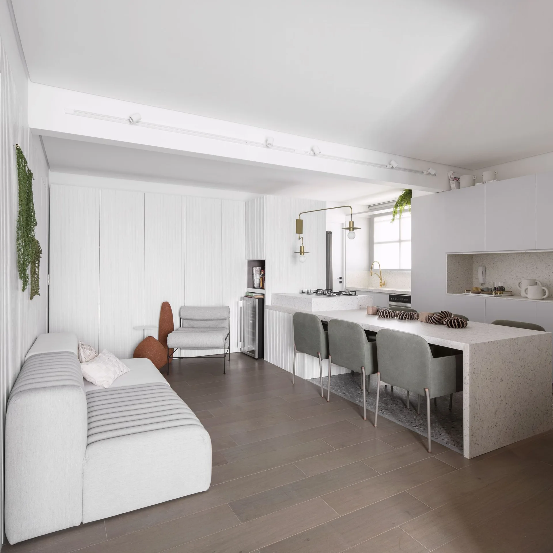 A contemporary kitchen and living space features a speckled stone island with green chairs, a low grey sofa, and white slatted wall paneling.