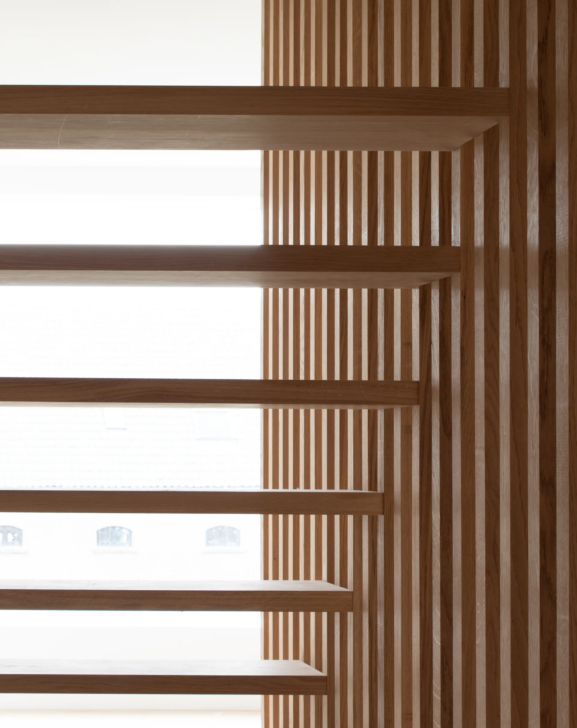 A minimalist wood staircase featuring floating treads set against a vertical slatted timber accent wall with bright natural light behind them.