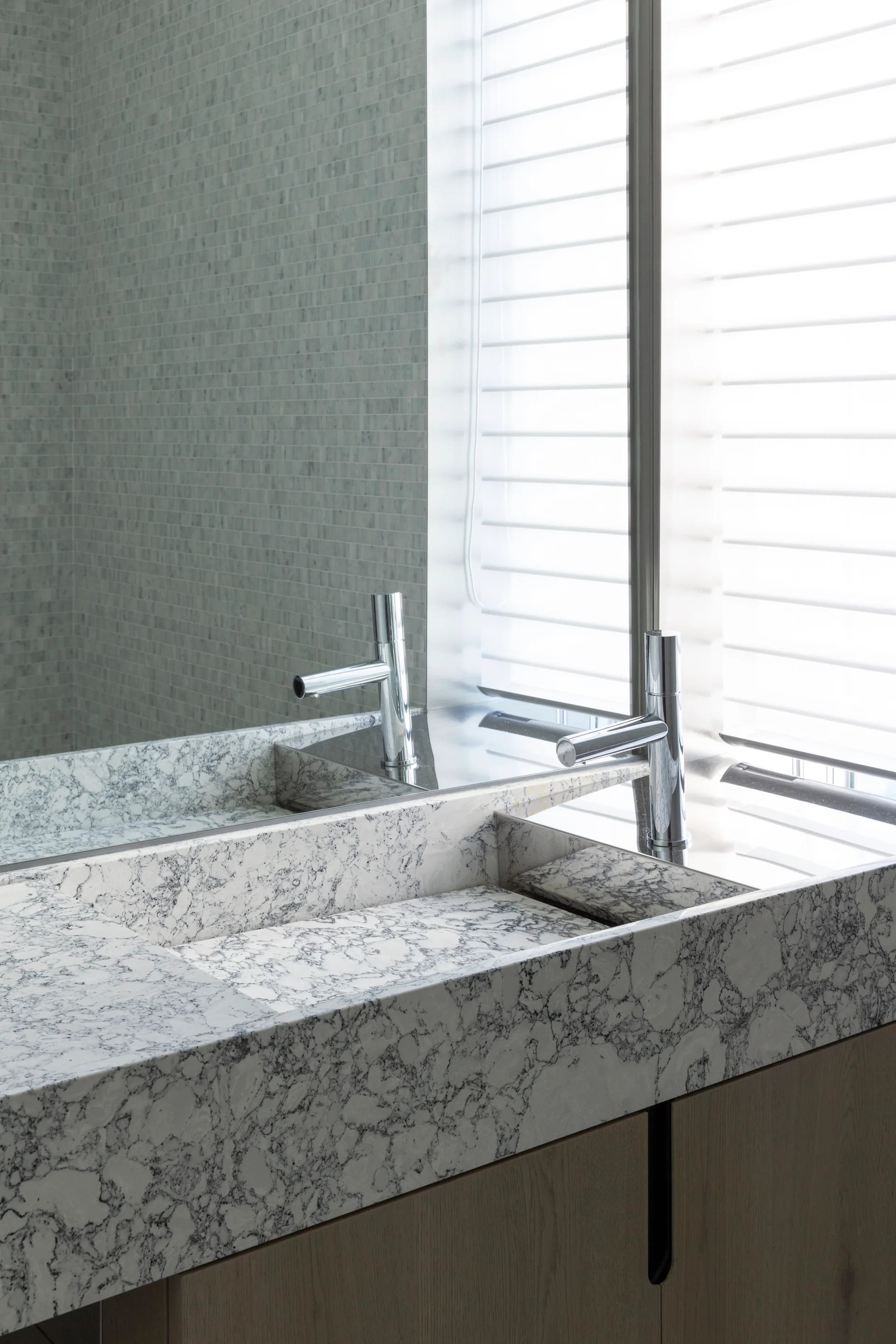 A modern bathroom vanity features an integrated grey and white marbled stone sink, a polished chrome faucet, and wood cabinetry beside a window.