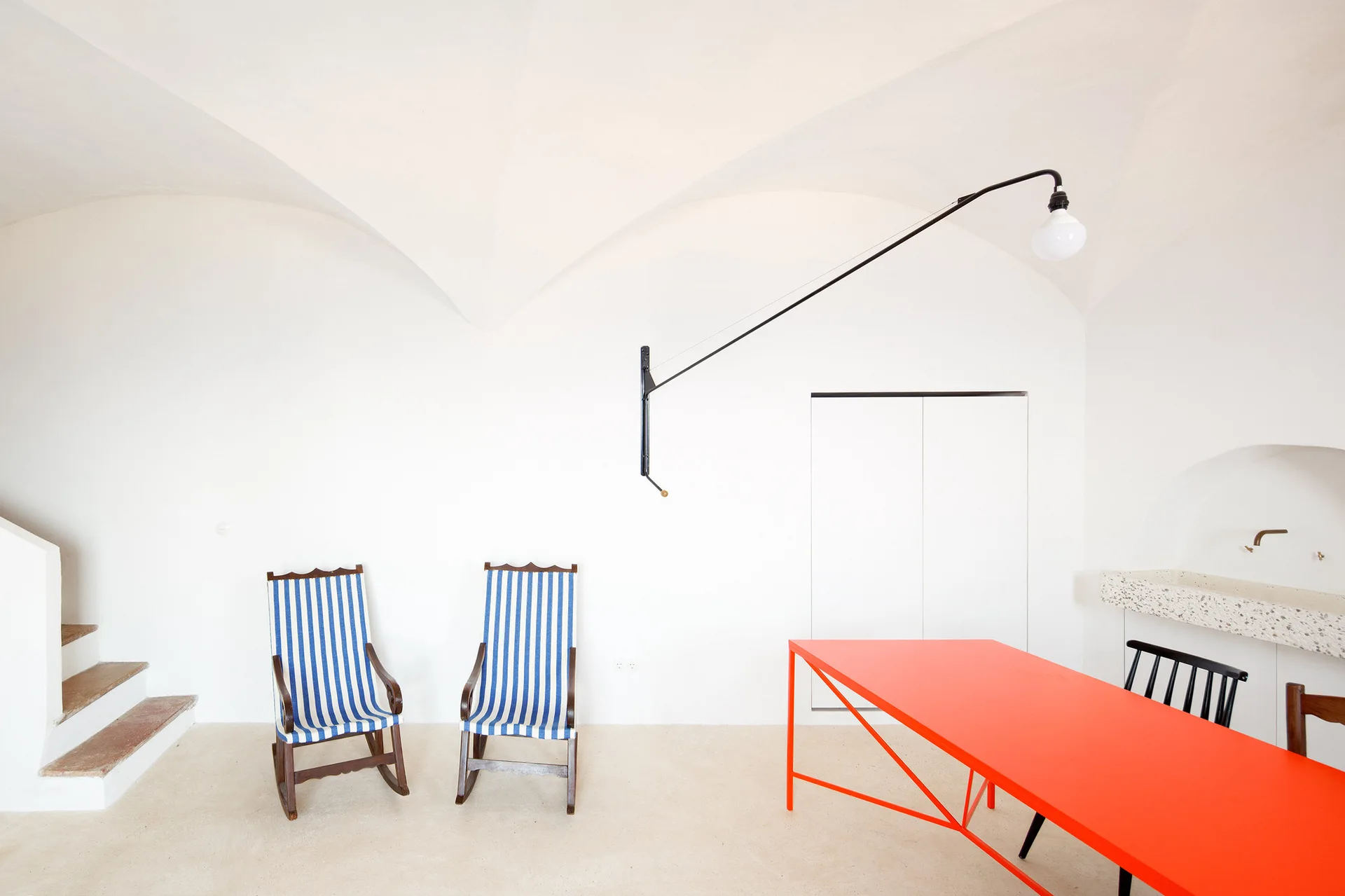 A bright room with a white vaulted ceiling, featuring two blue and white striped rocking chairs and a vibrant red dining table.