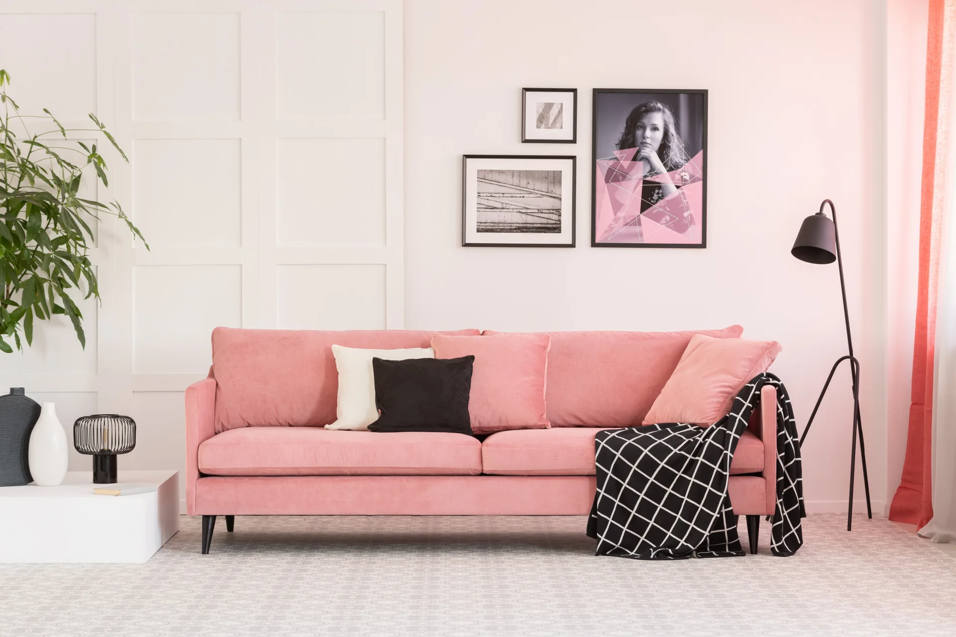 A modern pink velvet sofa is decorated with black and white cushions against a classic white paneled wall.