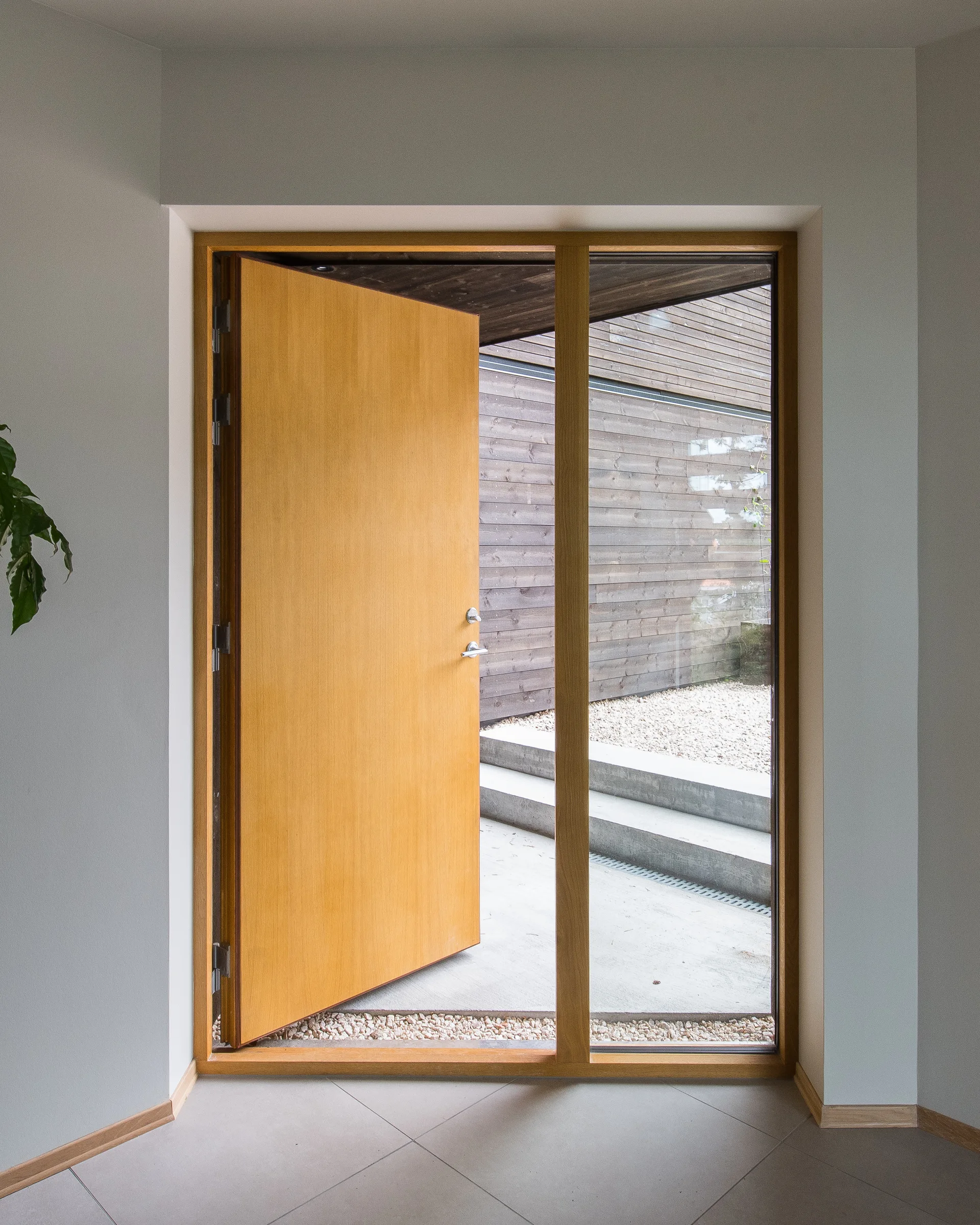 A light gray tiled entryway features a partially open warm wood door next to a matching glass sidelight looking out to concrete steps.