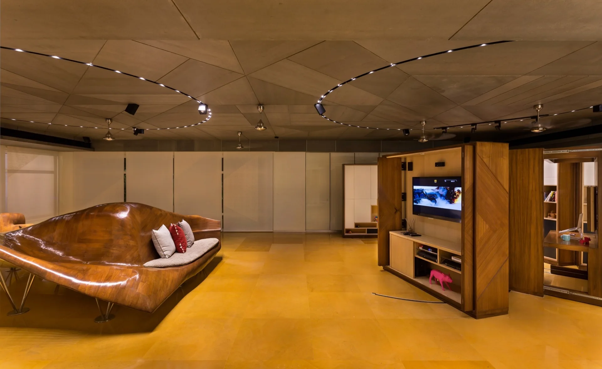 A spacious living area features a custom sculptural wooden sofa, an amber tiled floor, and a geometric panel ceiling with circular track lights.