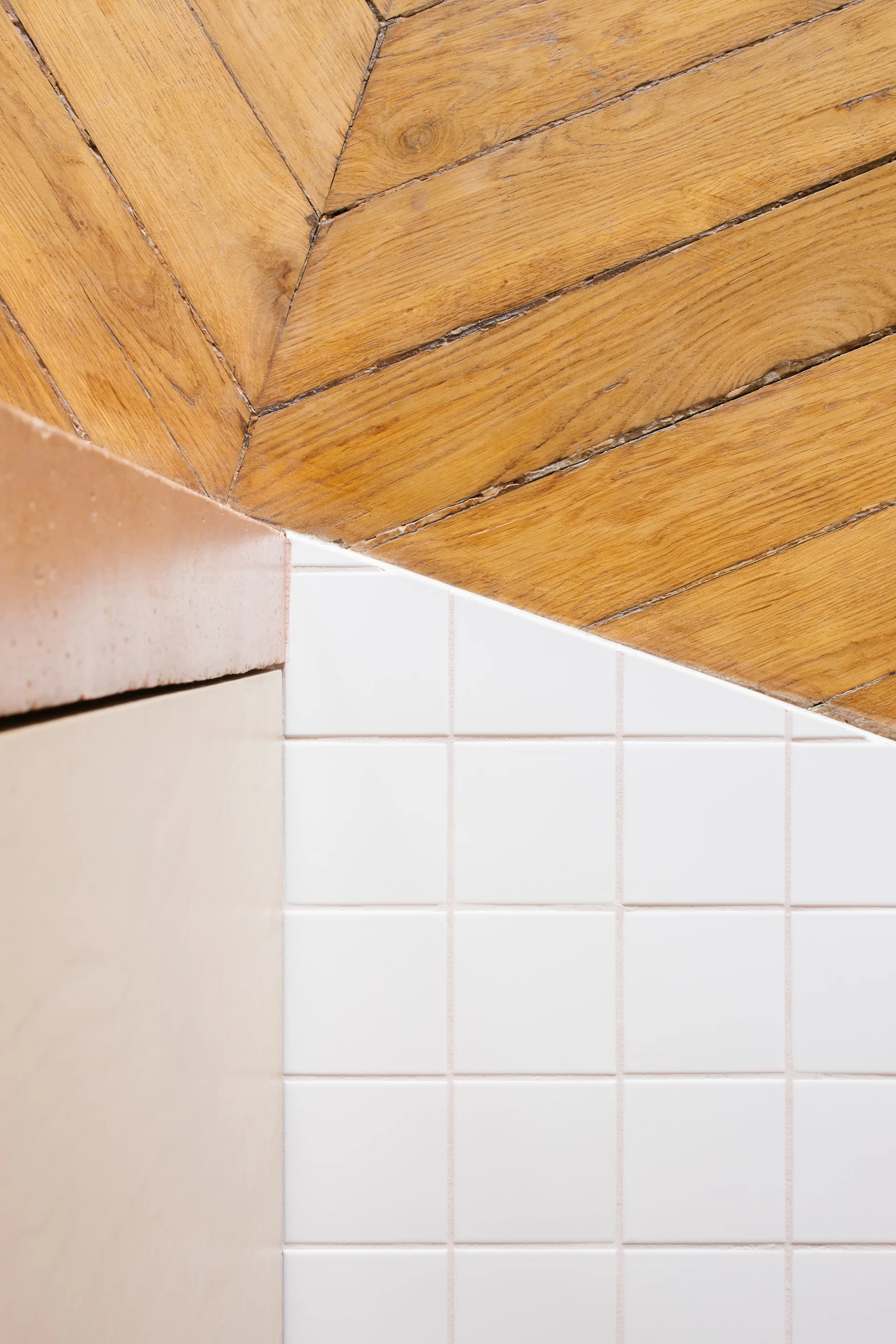 A close-up view showing a diagonal ceiling of chevron wood planks meeting a white square tiled wall next to a light wood cabinet.