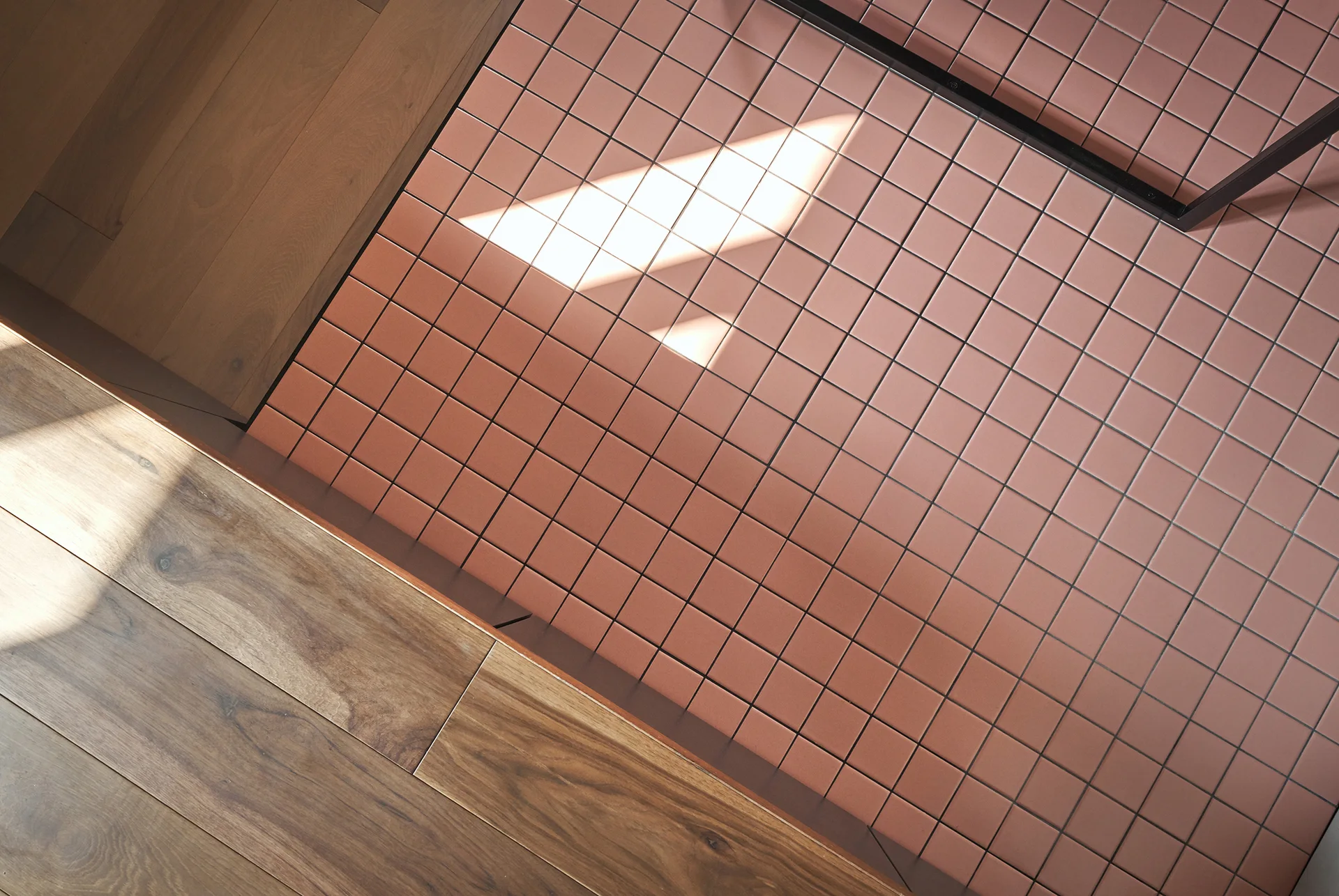 An overhead view shows a clean transition between a pink square mosaic tile floor and warm brown wood plank flooring.