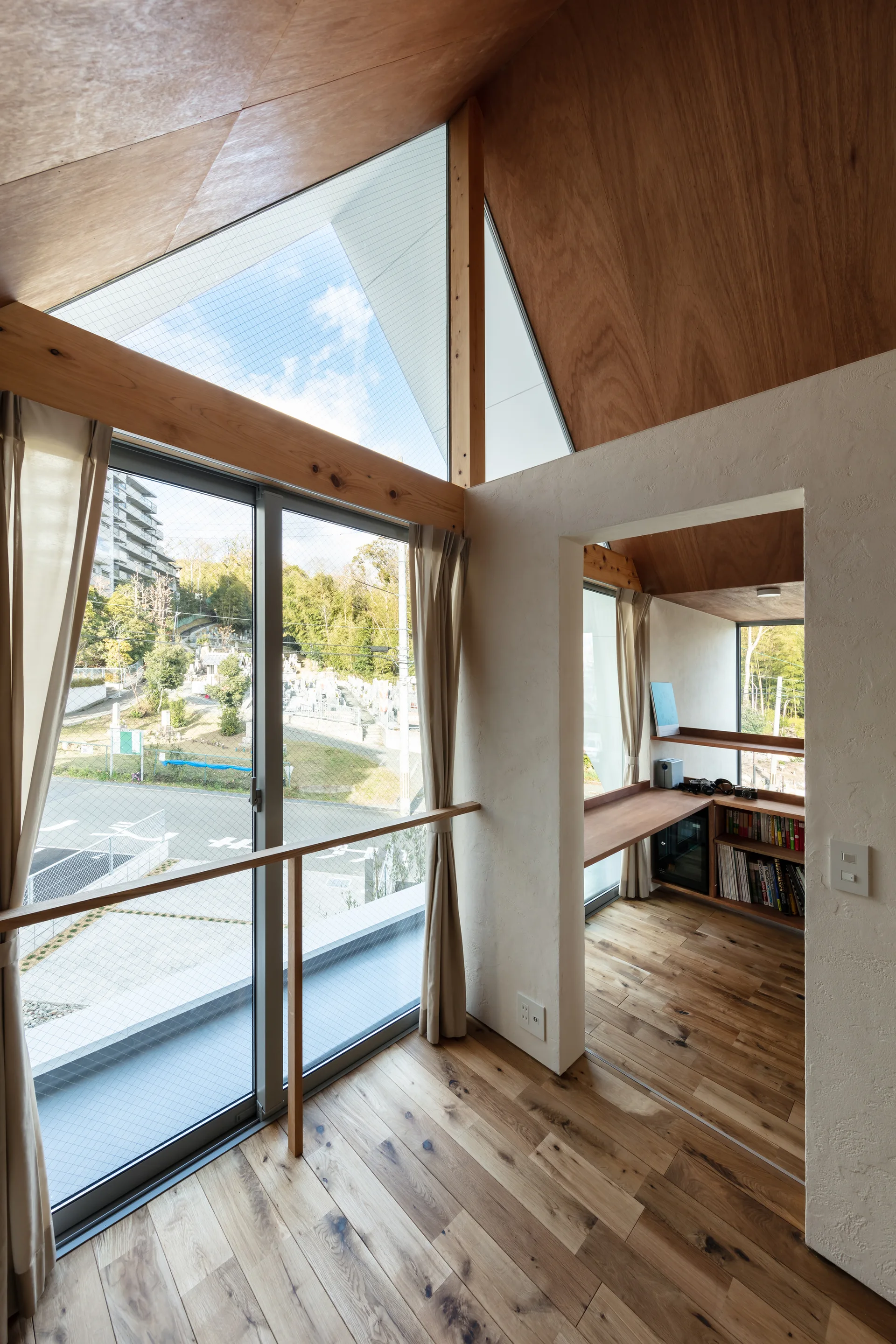 A minimalist study nook features a built-in wooden desk, hardwood floors, and a vaulted plywood ceiling next to a sliding glass door.