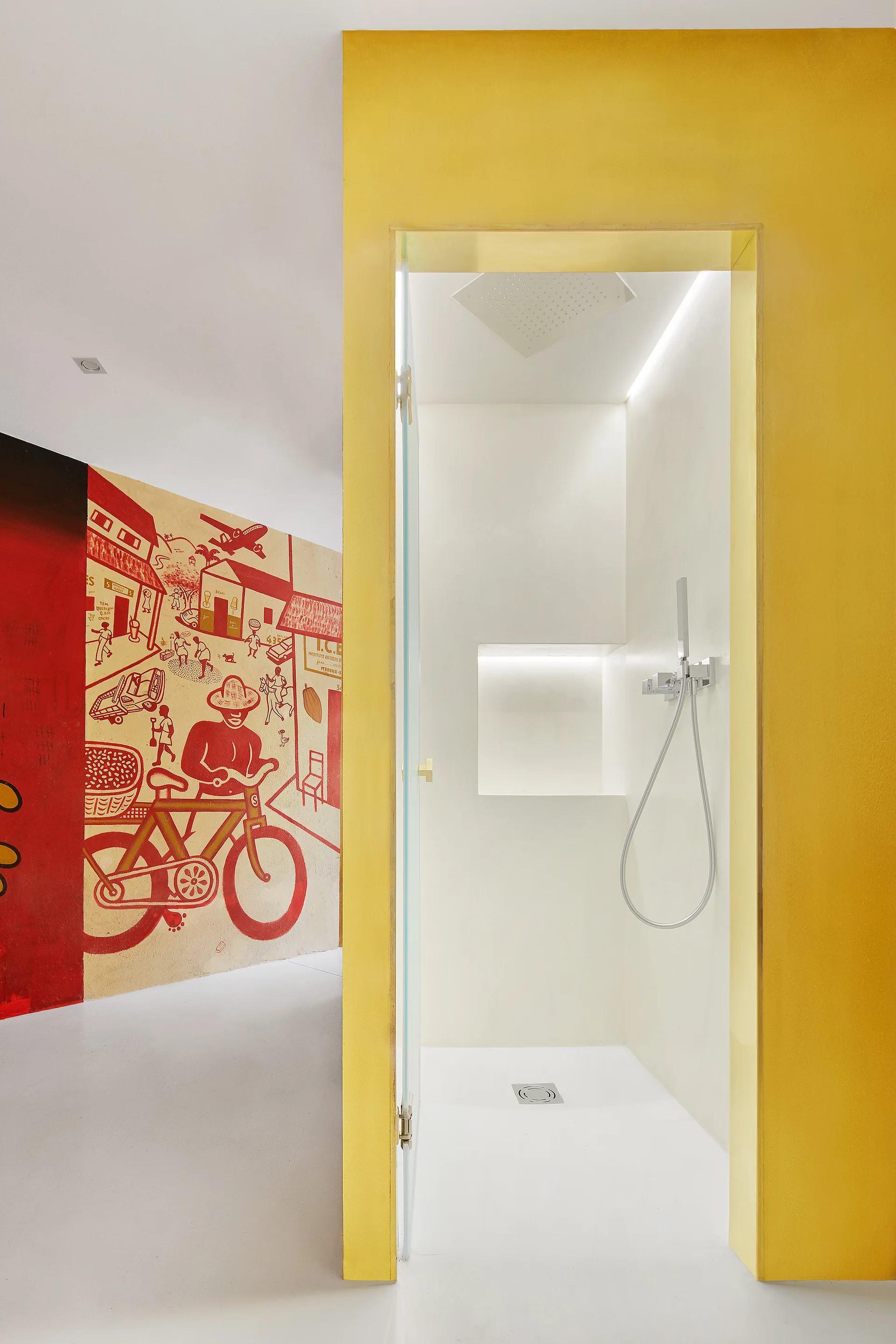 A modern walk-in shower framed in bright yellow sits next to a white wall featuring a large red and cream mural of a person on a bicycle.