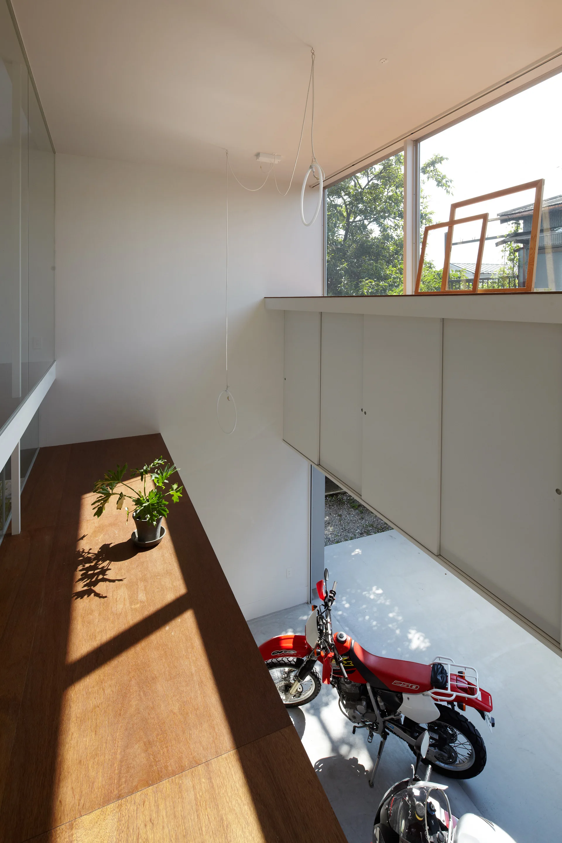 An elevated wooden mezzanine with a small potted plant overlooks a concrete garage with a parked red motorcycle and white built-in cabinets.