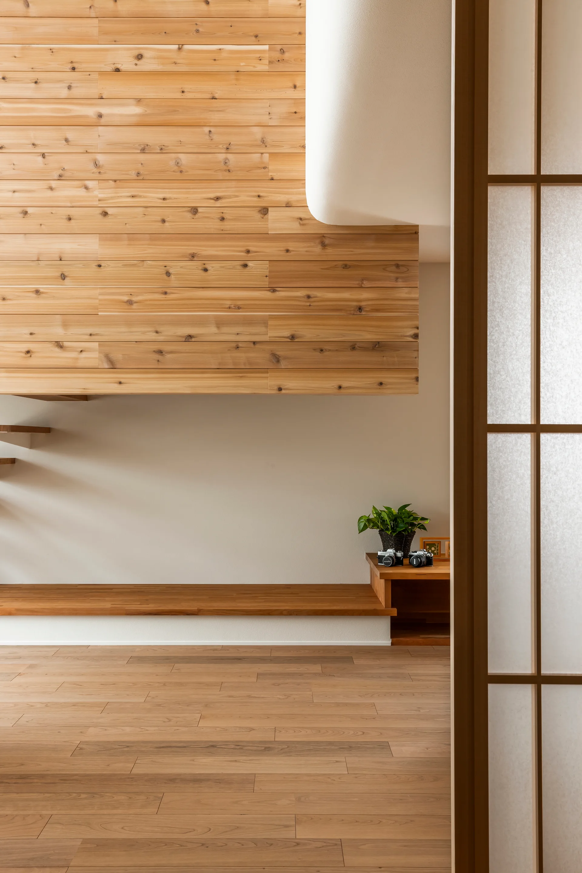 A minimalist room features light wood floor planks, a horizontal wood-paneled wall section, a low-slung floating bench, and a translucent shoji screen.