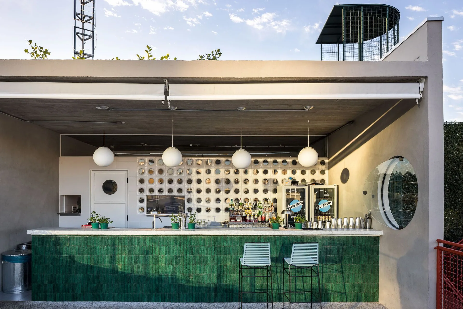 An outdoor rooftop bar features an emerald green tiled counter, four spherical globe pendant lights, and a patterned back wall.
