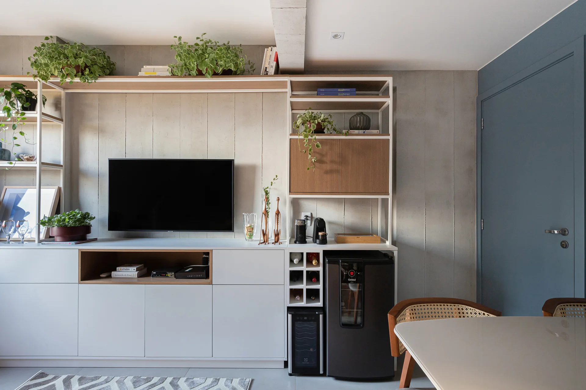 A custom white and wood built-in media unit displays a television and potted plants next to an integrated beverage cooler against a textured gray wall.