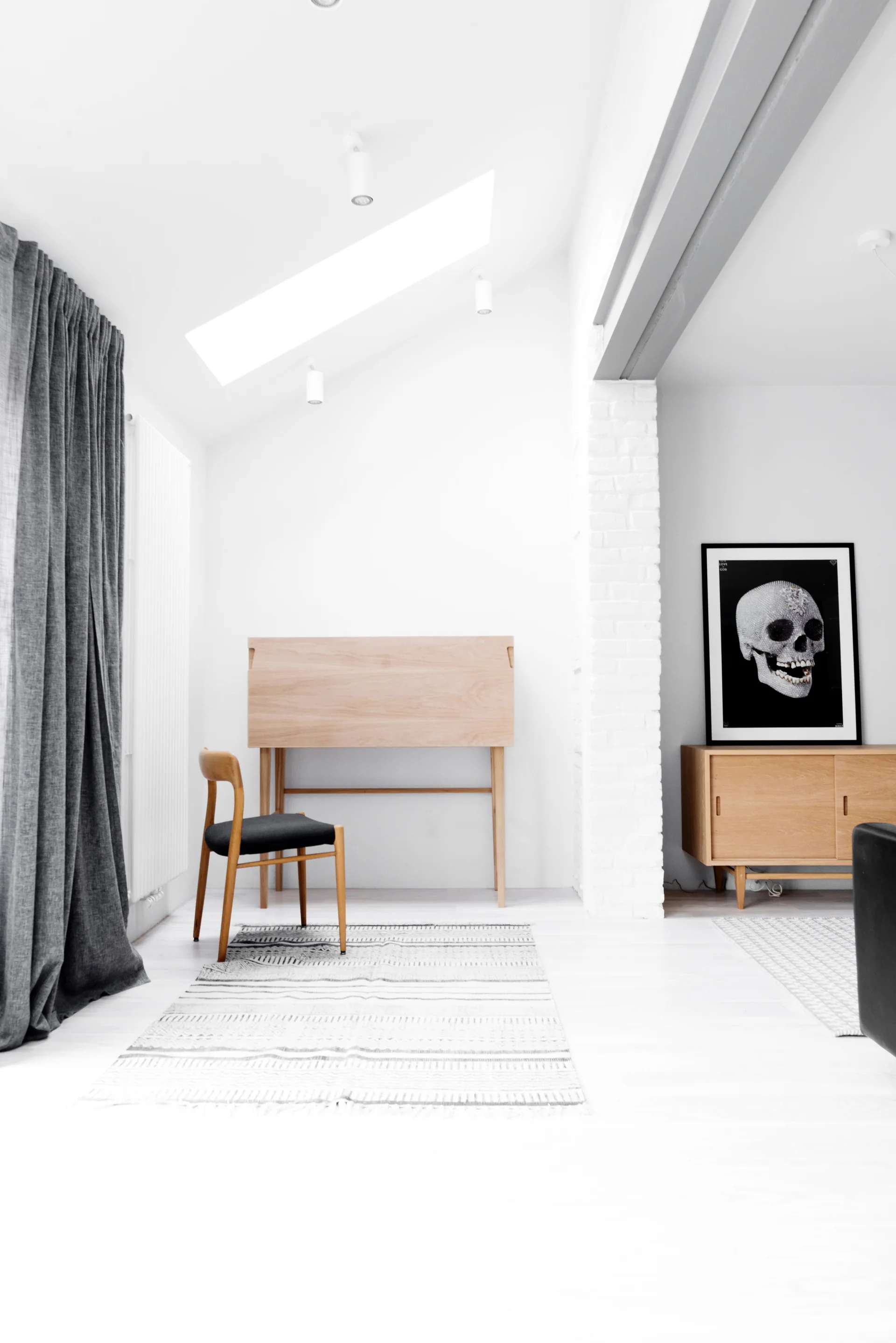 A minimalist home office featuring a light wood desk and chair on a patterned rug under a slanted ceiling with a skylight.