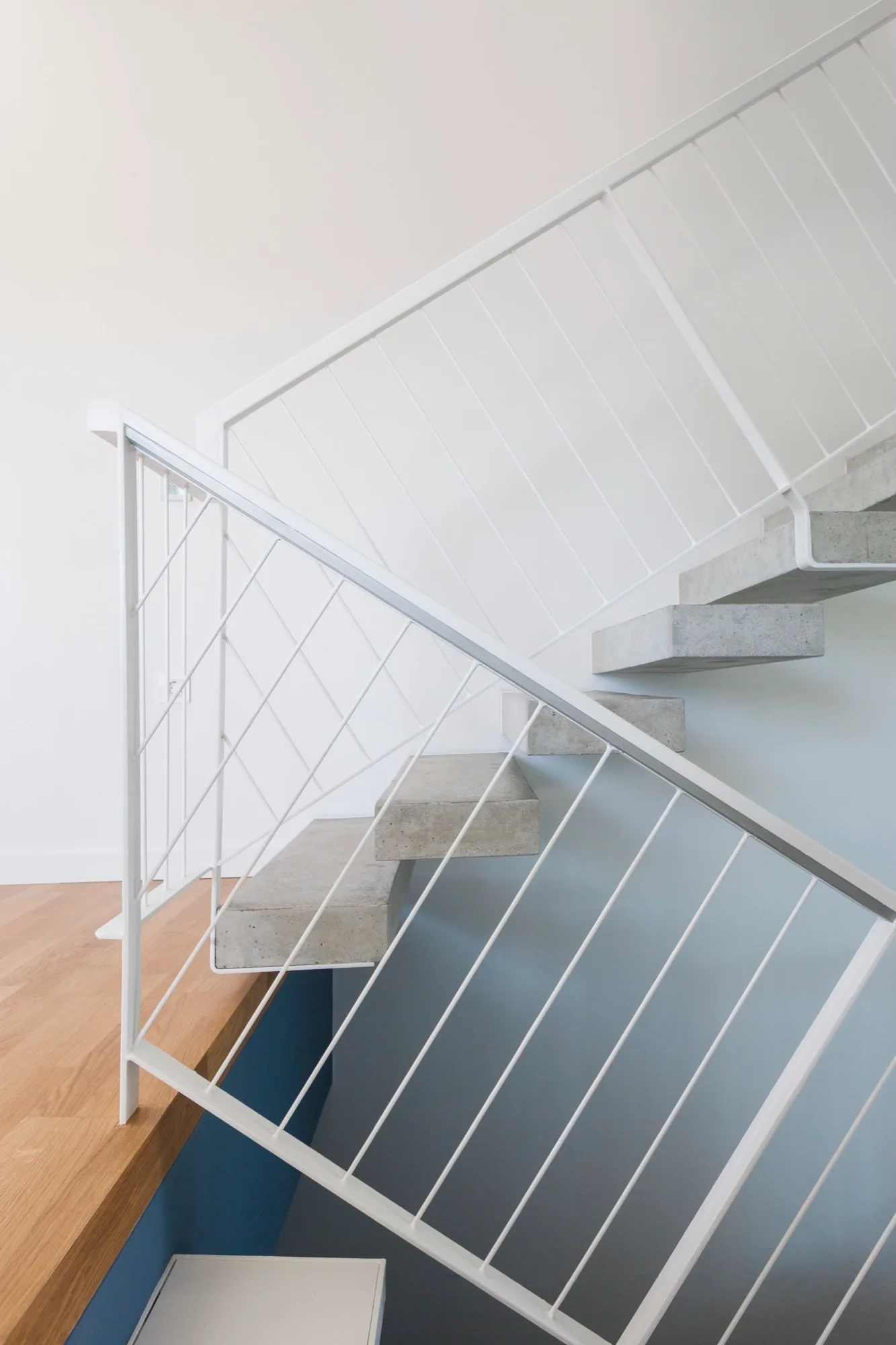 A modern floating staircase features cantilevered concrete treads and a white geometric metal handrail against a solid white wall.