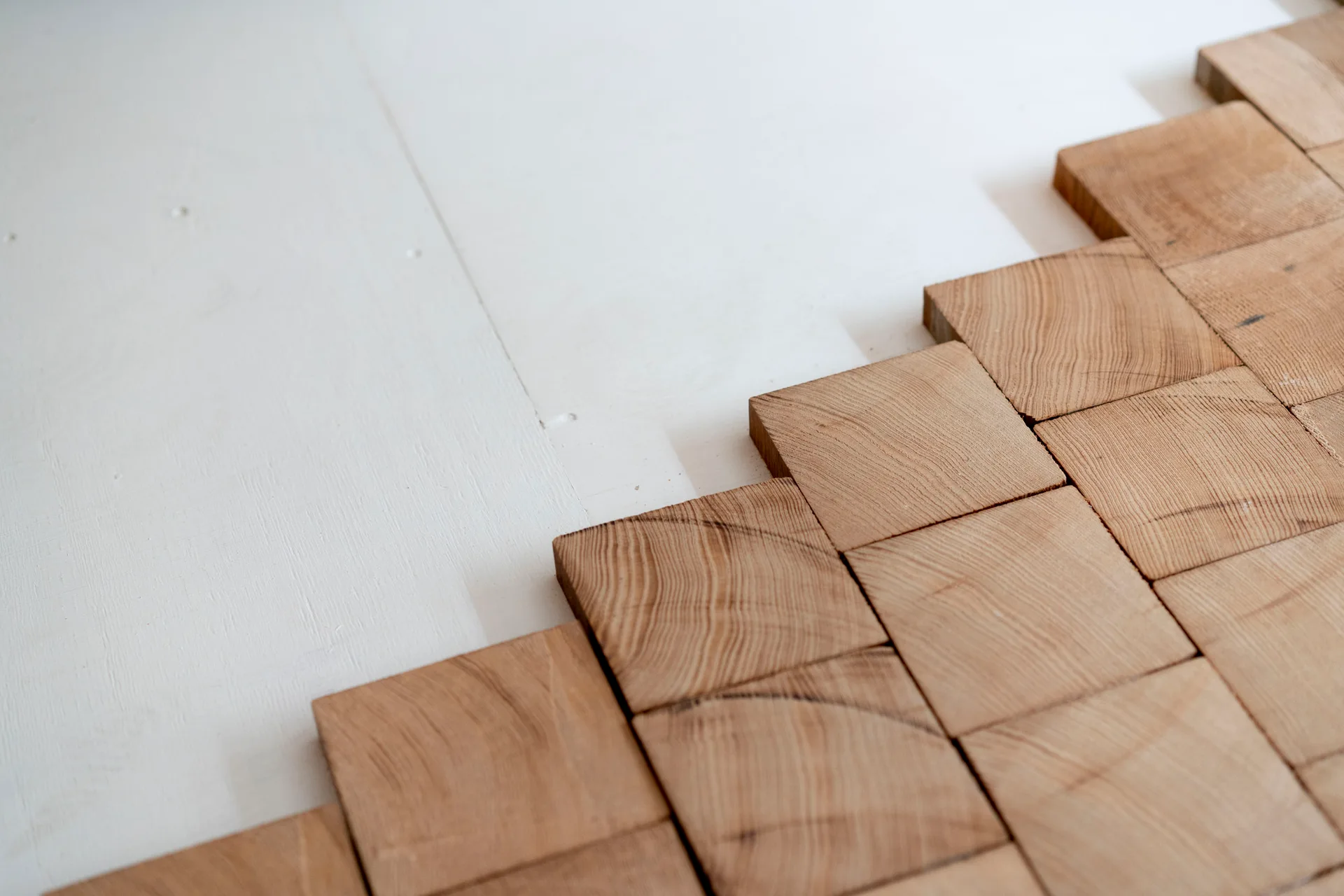 Square wooden blocks with visible end-grain patterns are laid diagonally on a flat white subfloor during installation.