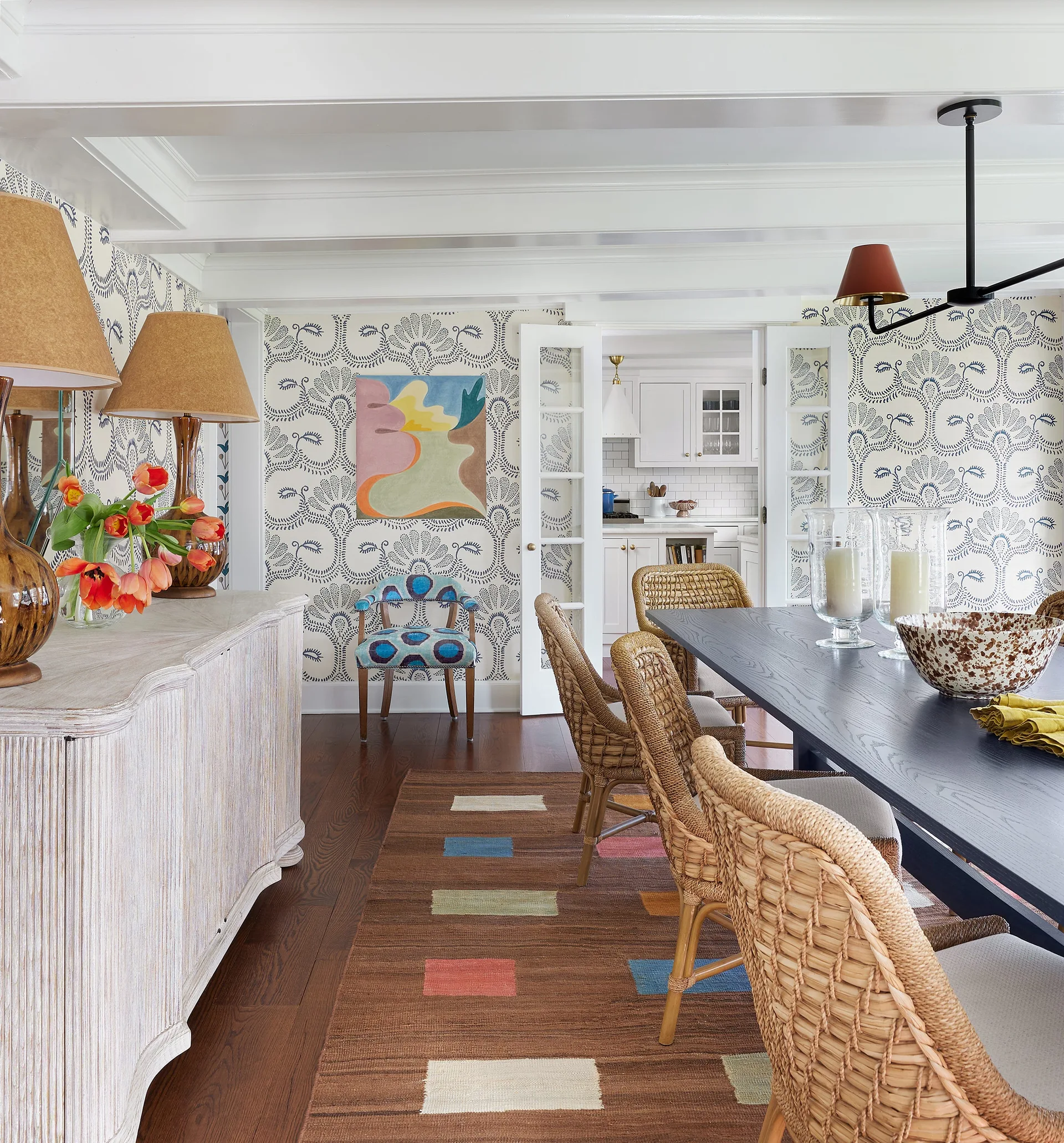 A dining room featuring blue and white botanical wallpaper, woven rattan chairs around a dark table, and a light wood sideboard.
