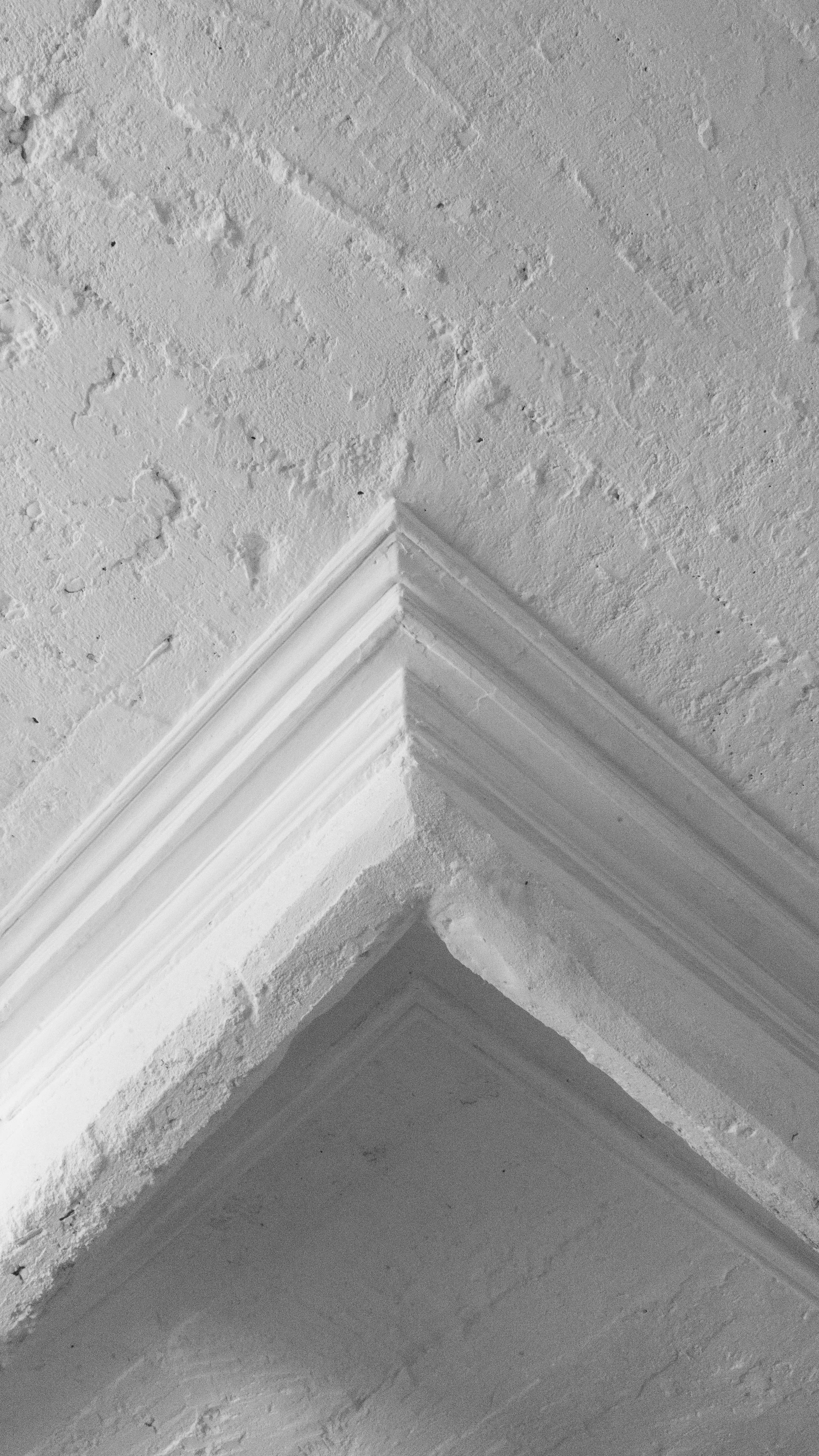 A close-up view of a rustic white plaster ceiling corner highlighted by a stepped architectural crown molding with a matte finish.