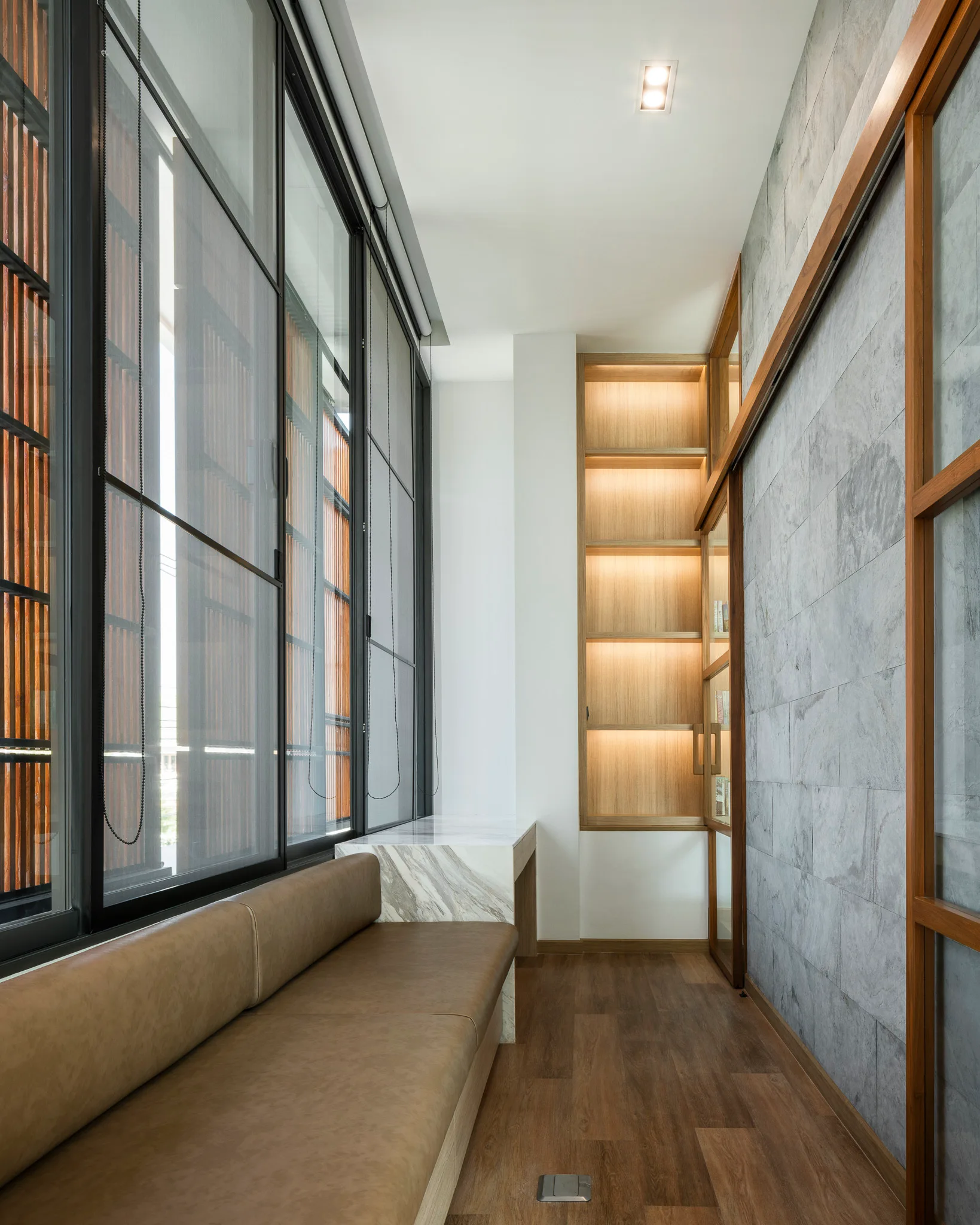 A modern corridor featuring a built-in brown leather bench, a grey stone accent wall, and wood display shelves with integrated warm lighting.