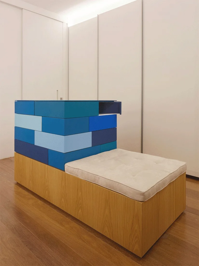 A minimalist wooden storage bench featuring a tufted beige cushion next to a modular stack of colorful blue storage drawers.