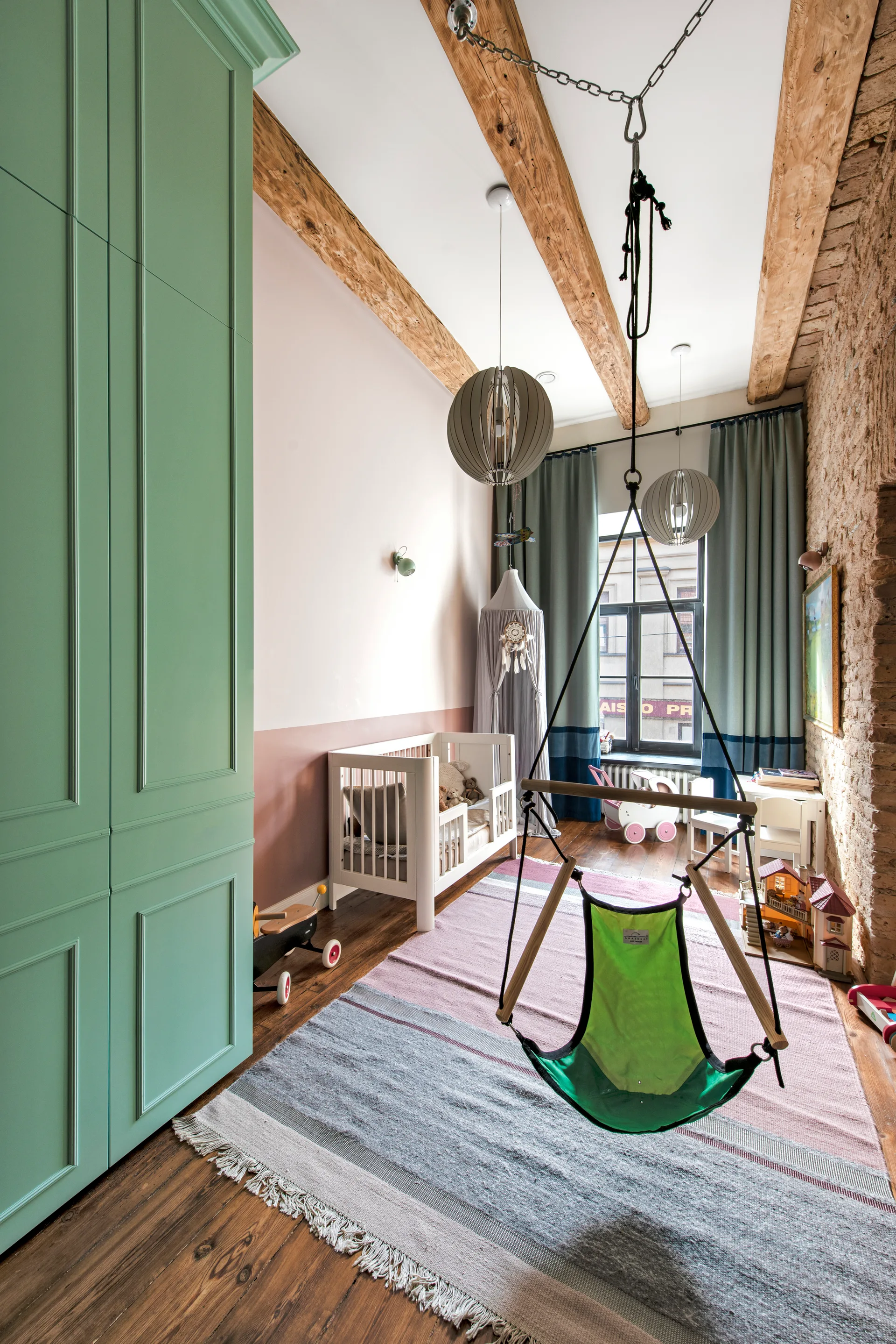 A nursery featuring a large mint green wardrobe, a white crib, a suspended green swing, and exposed wooden ceiling beams.