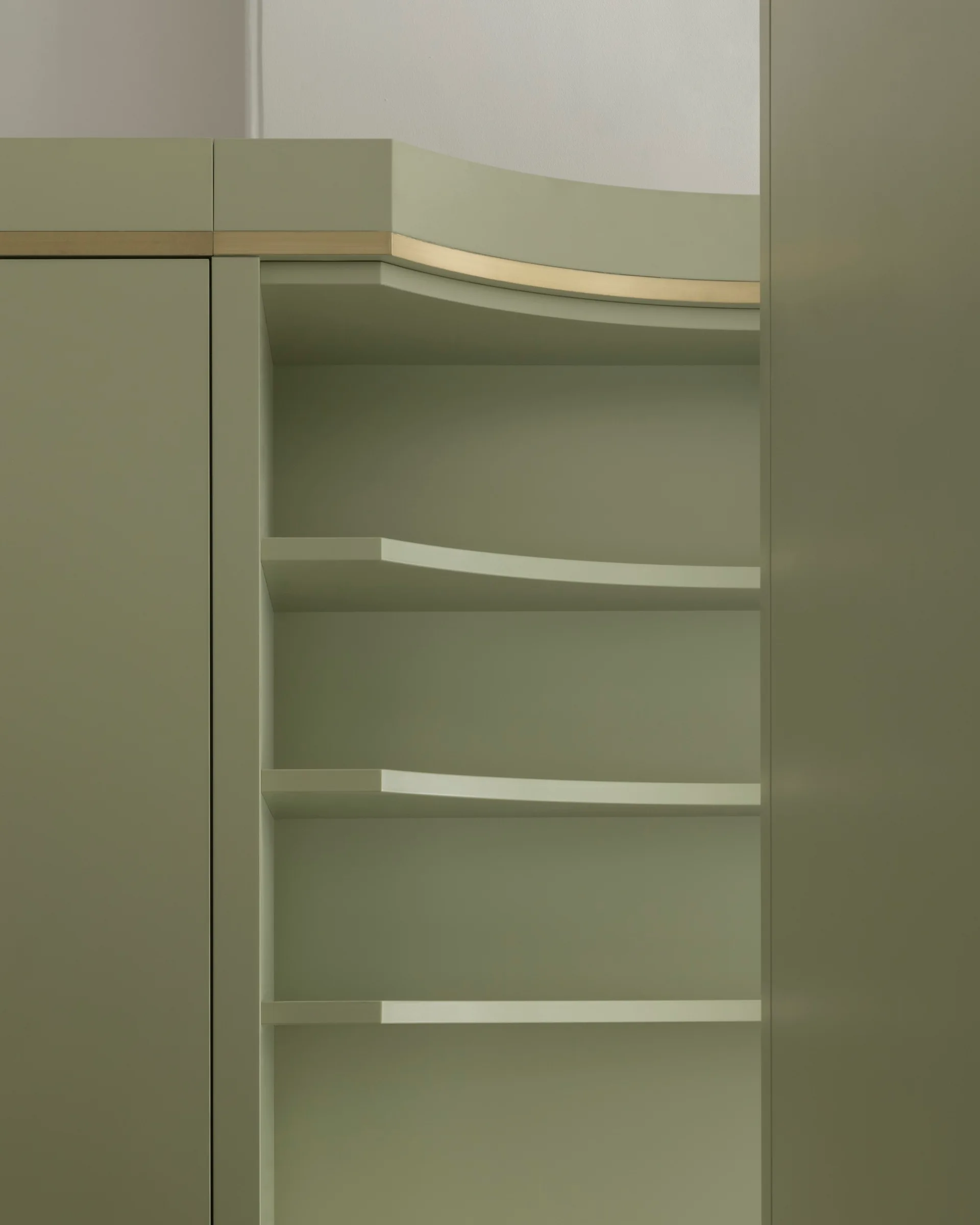 Close-up of sage green built-in cabinets featuring open curved shelves and a thin gold-toned metallic trim line along the top edge.