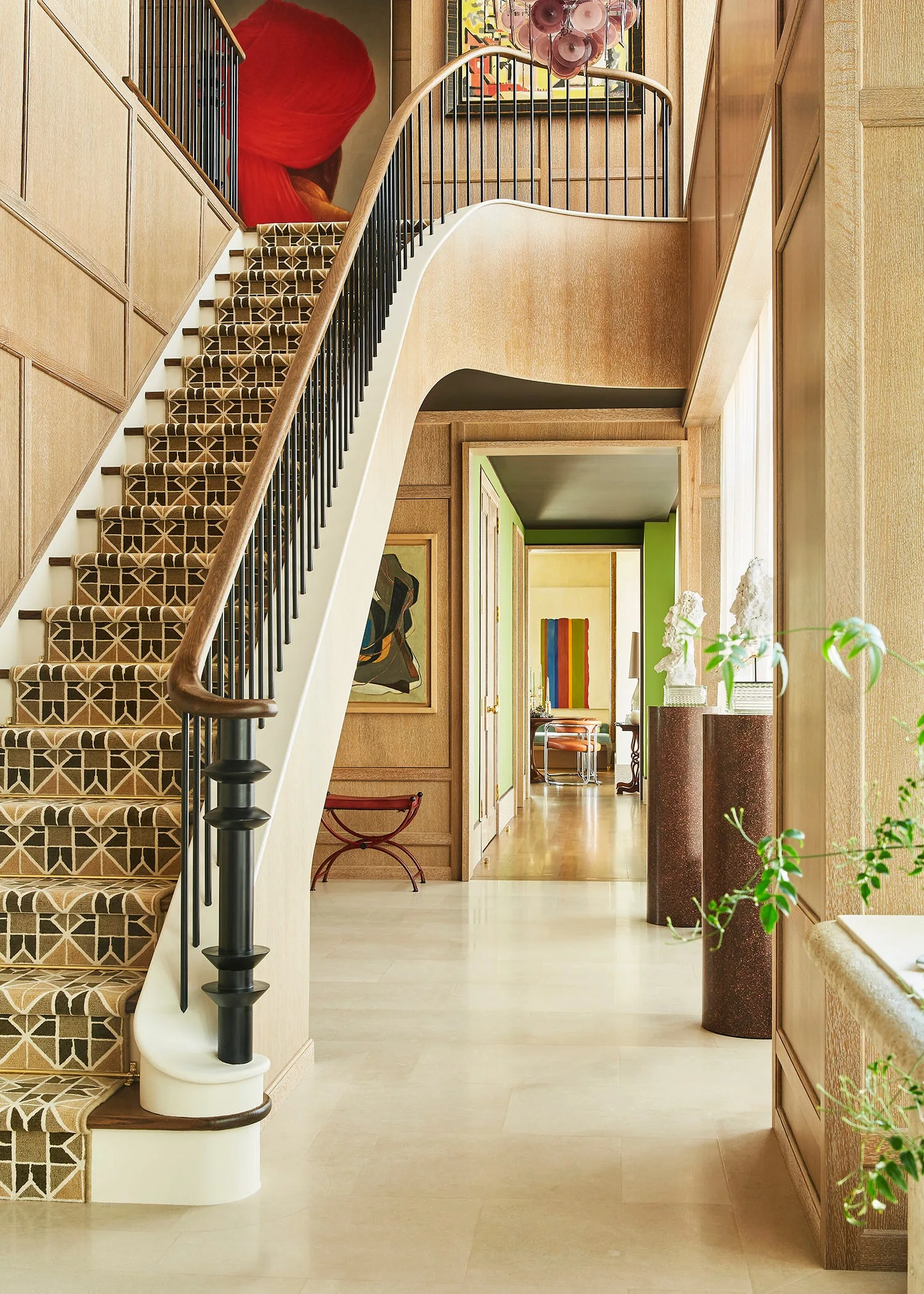 A light wood-paneled entryway features a curved staircase with a brown geometric patterned runner leading toward a hallway with green walls.