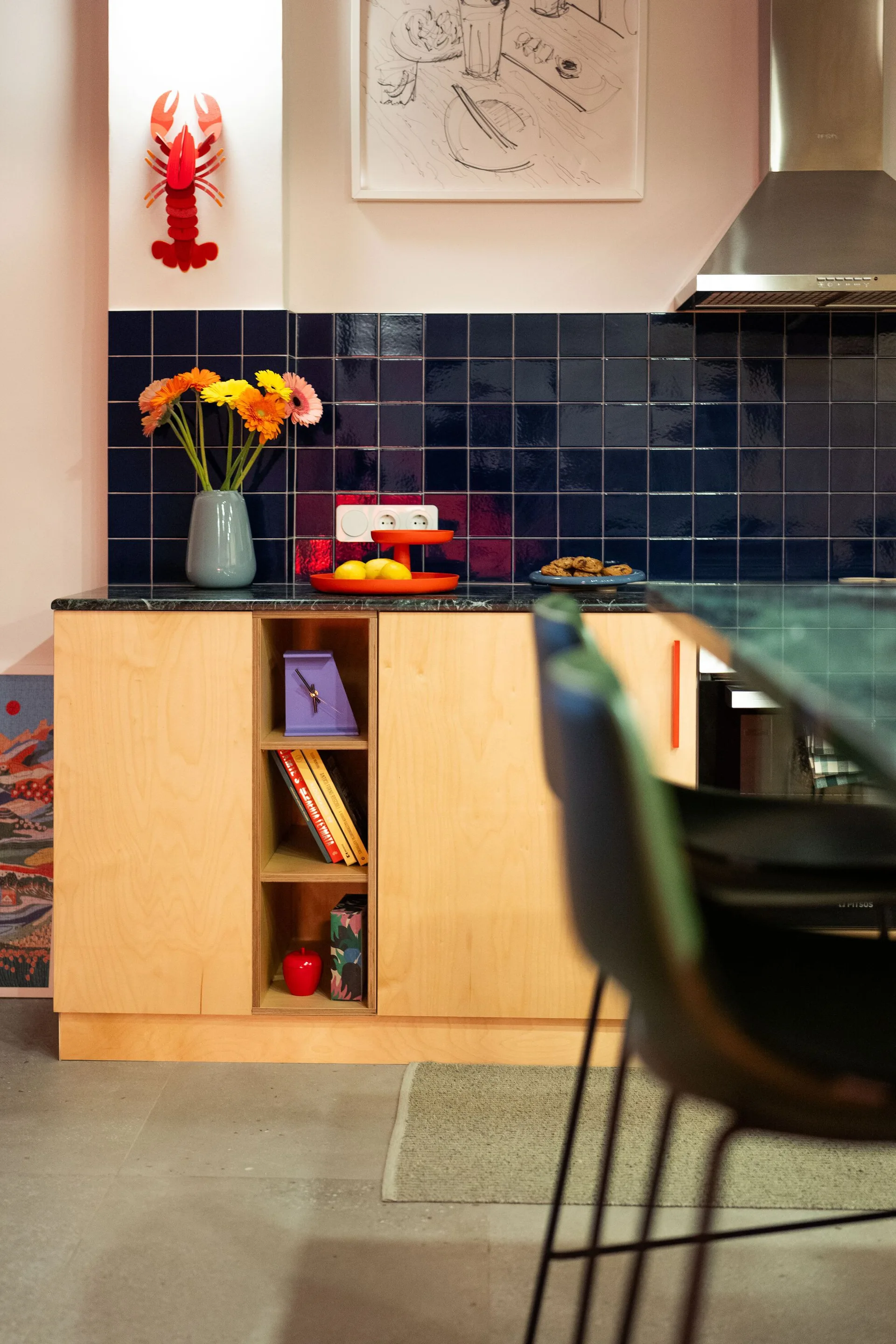 A modern kitchen features light wood cabinets with a dark stone countertop, an integrated open shelf, and a dark blue glossy tile backsplash.