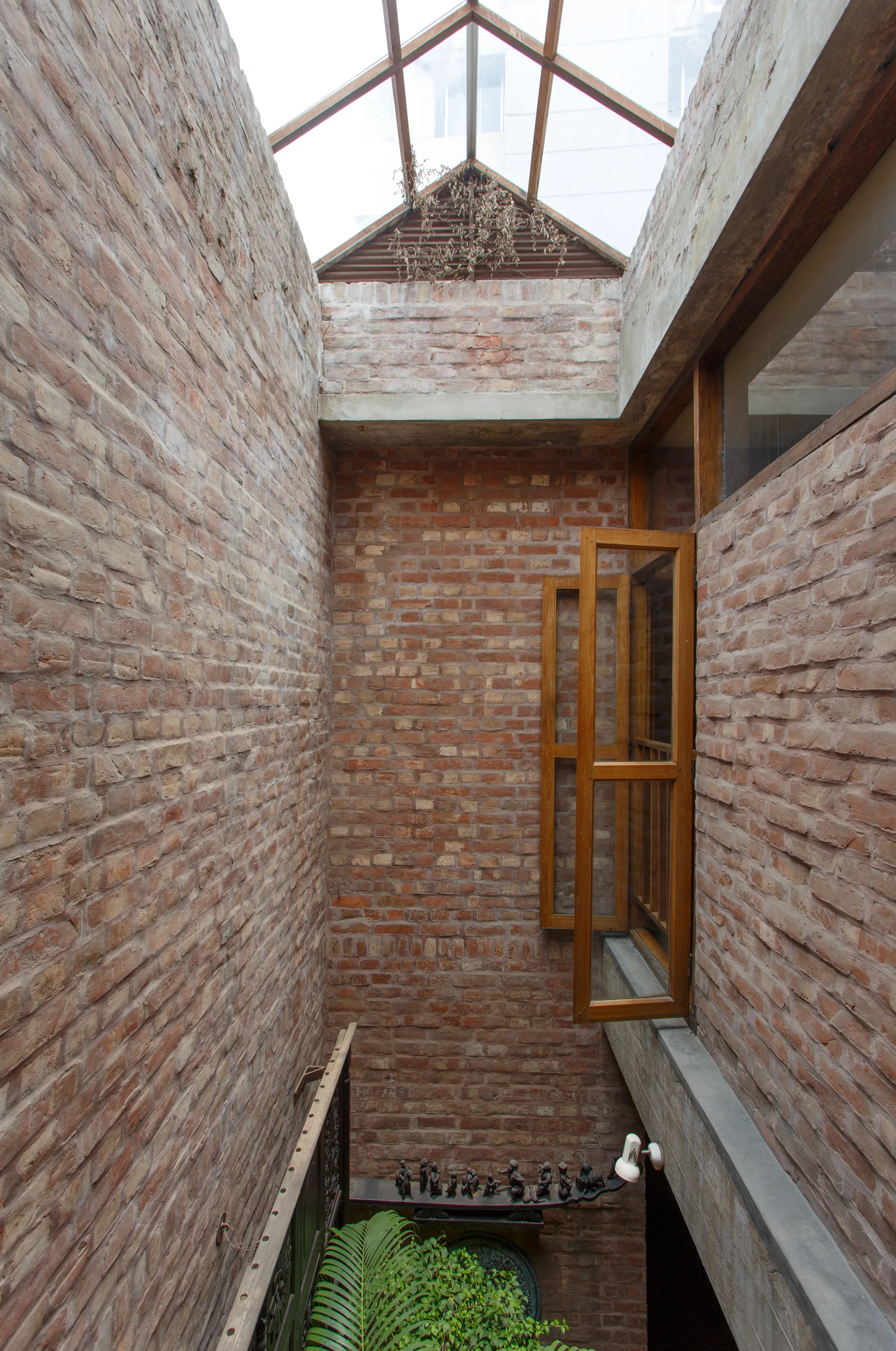 A tall brick stairwell features a peaked glass skylight and an open wood-framed casement window looking down into the narrow atrium.