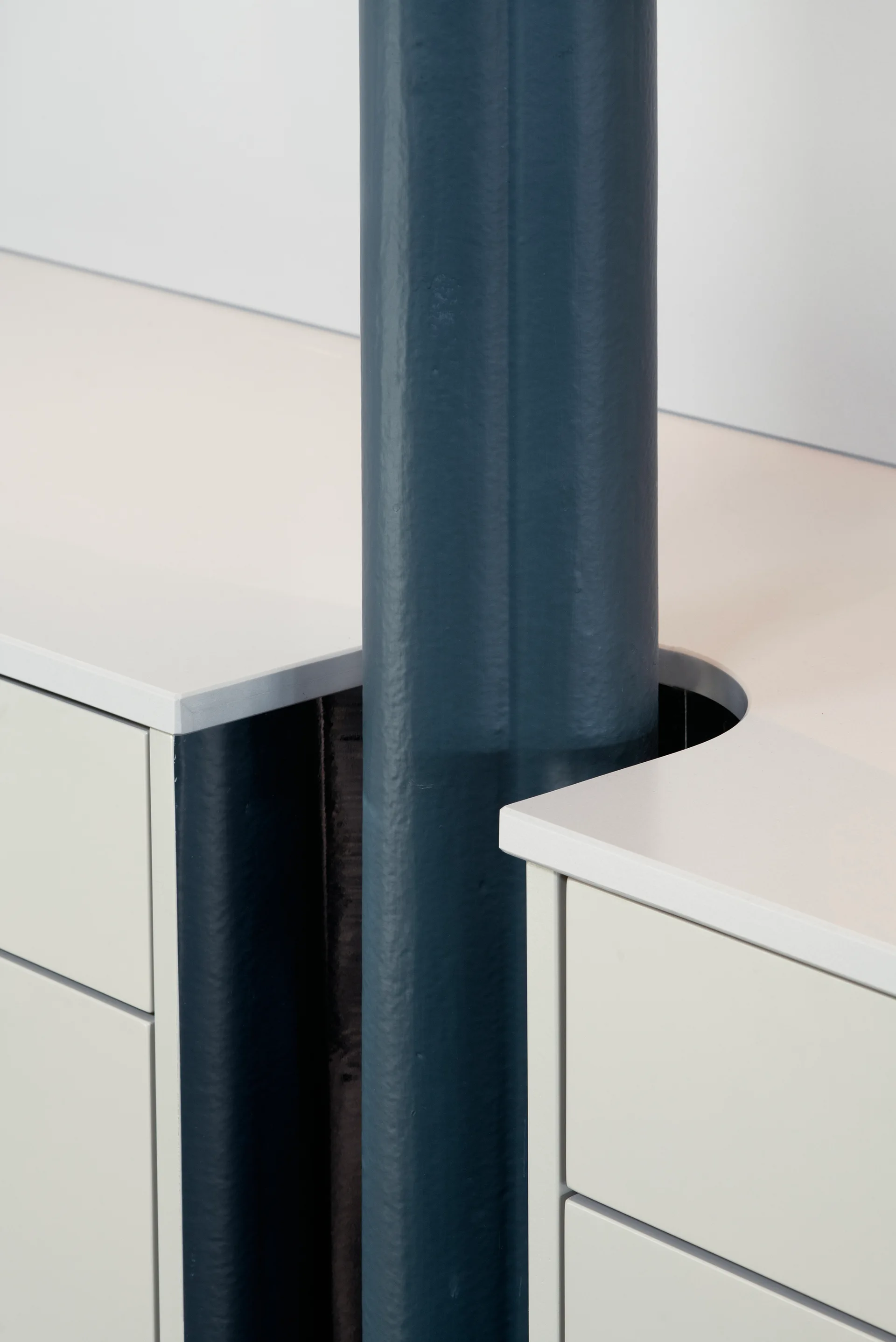 A close-up of a dark blue painted structural column integrated into off-white storage cabinetry with a custom curved countertop cutout.