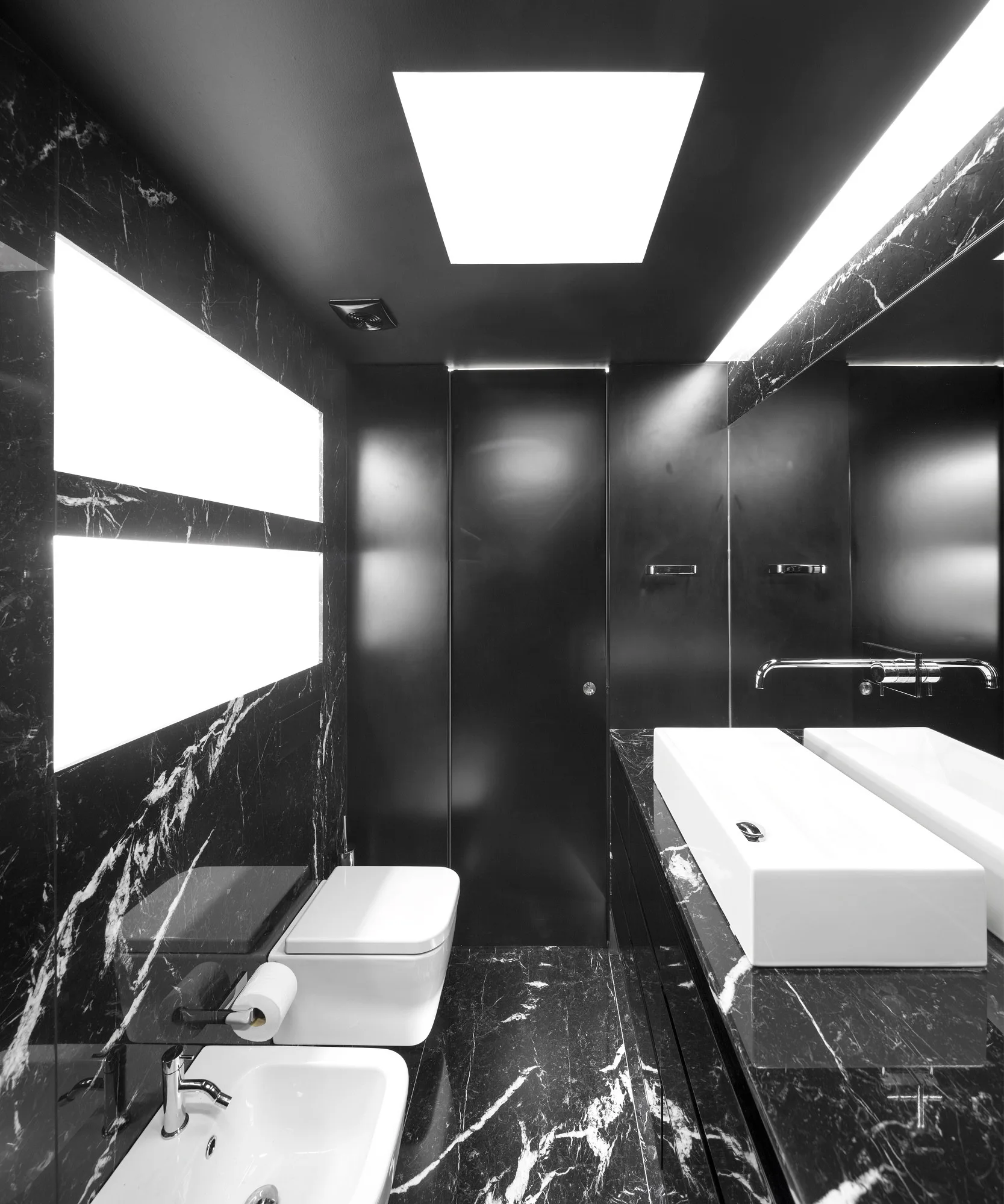 A contemporary bathroom features black veined marble walls and floors, a white toilet, bidet, and a rectangular vessel sink.