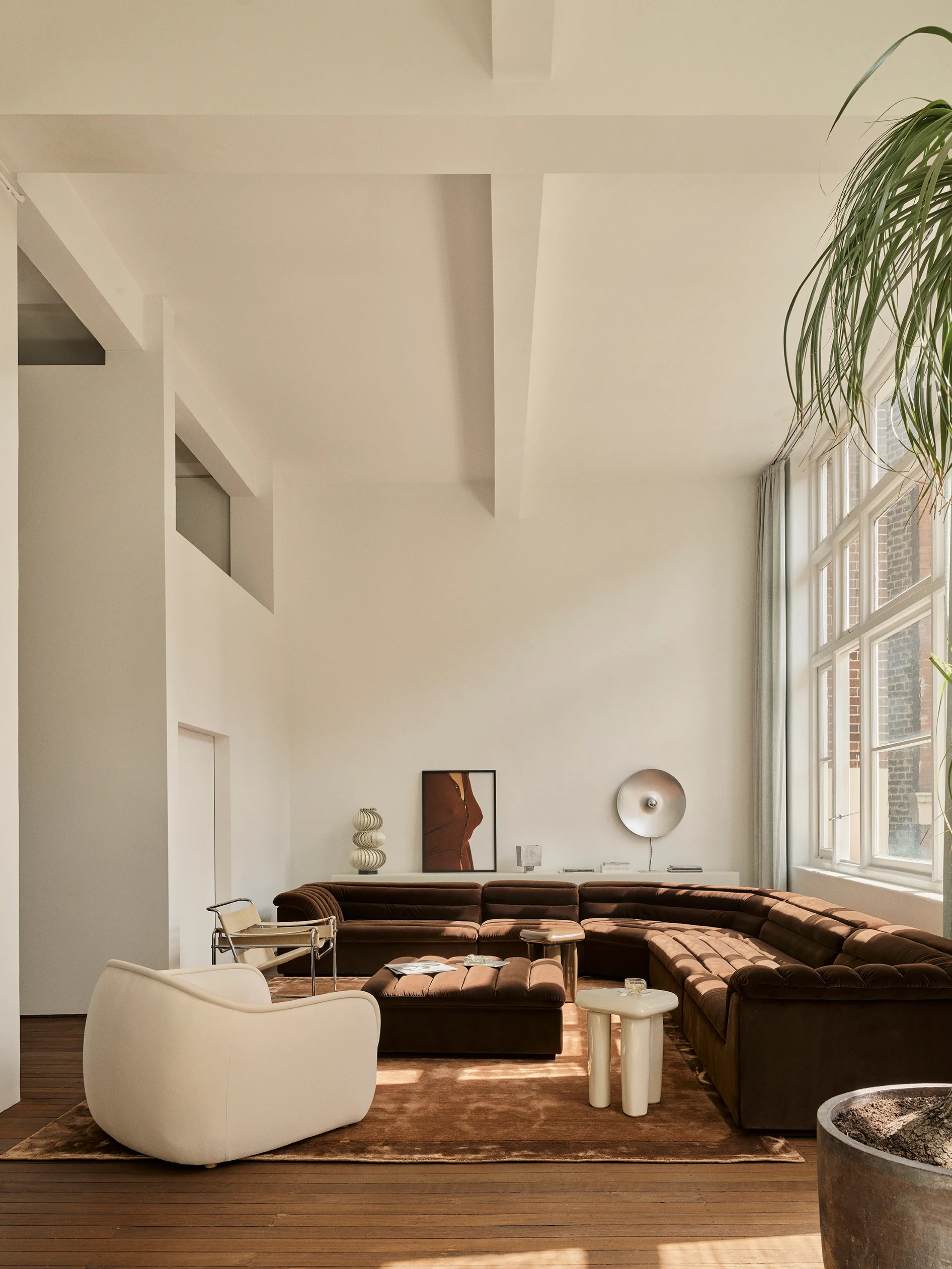 A spacious loft living room featuring a chocolate brown velvet sectional, a cream armchair, and white exposed ceiling beams.