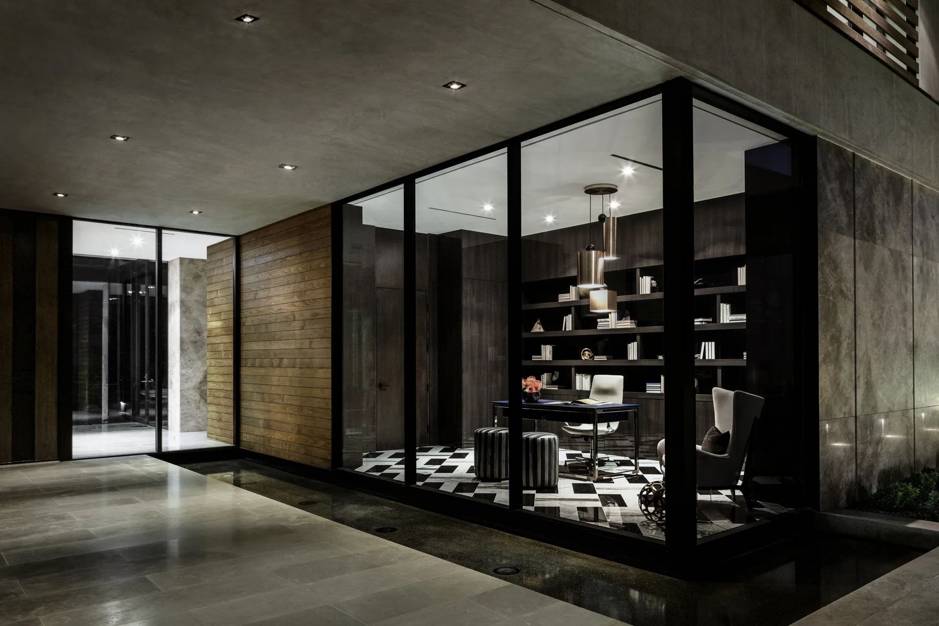 A contemporary glass-enclosed home office features a dark wood bookshelf, a central desk, and a bold black-and-white checkered floor.
