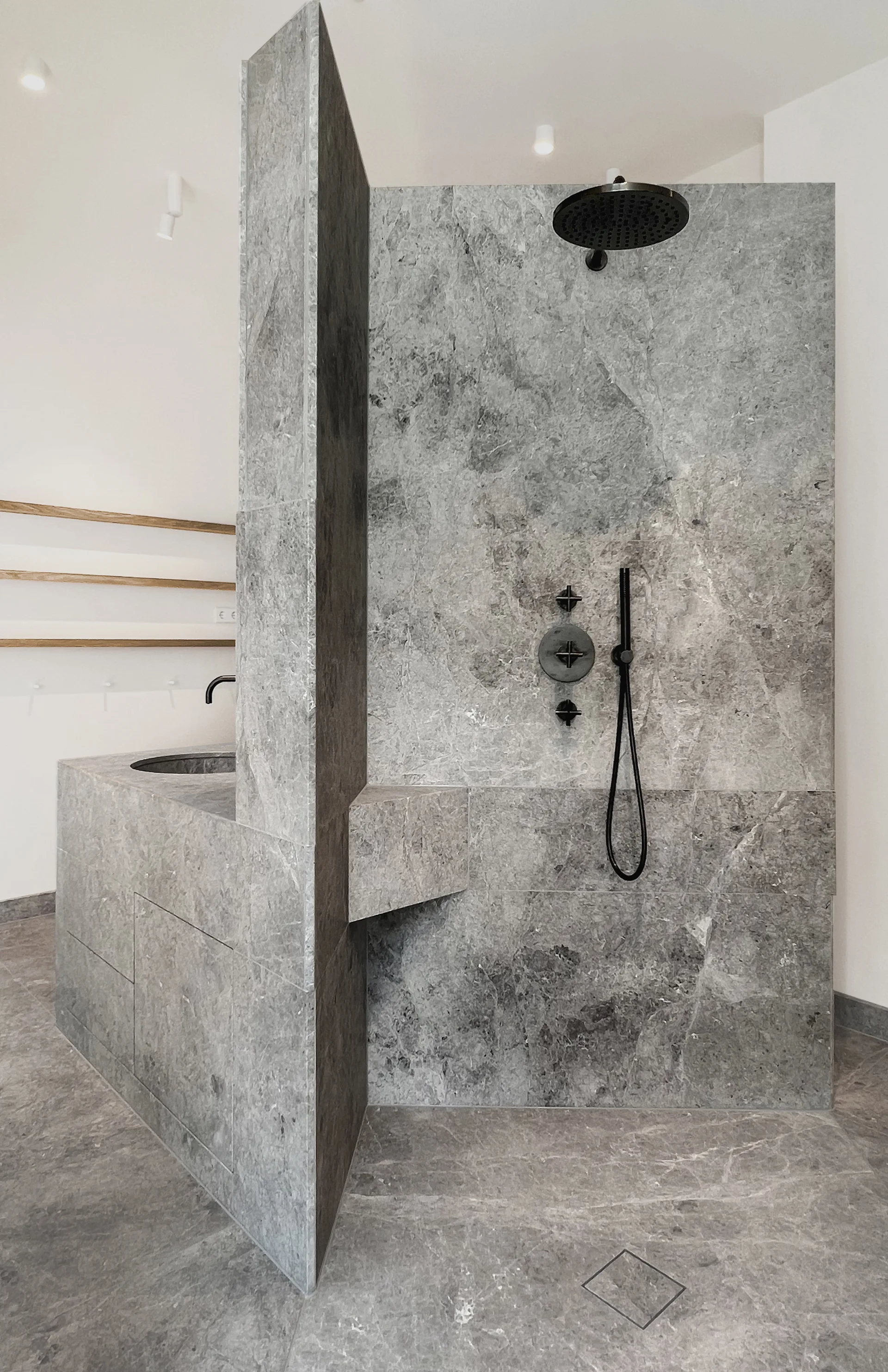 A modern bathroom features a large grey stone partition separating a walk-in shower with matte black fixtures from an integrated stone vanity.