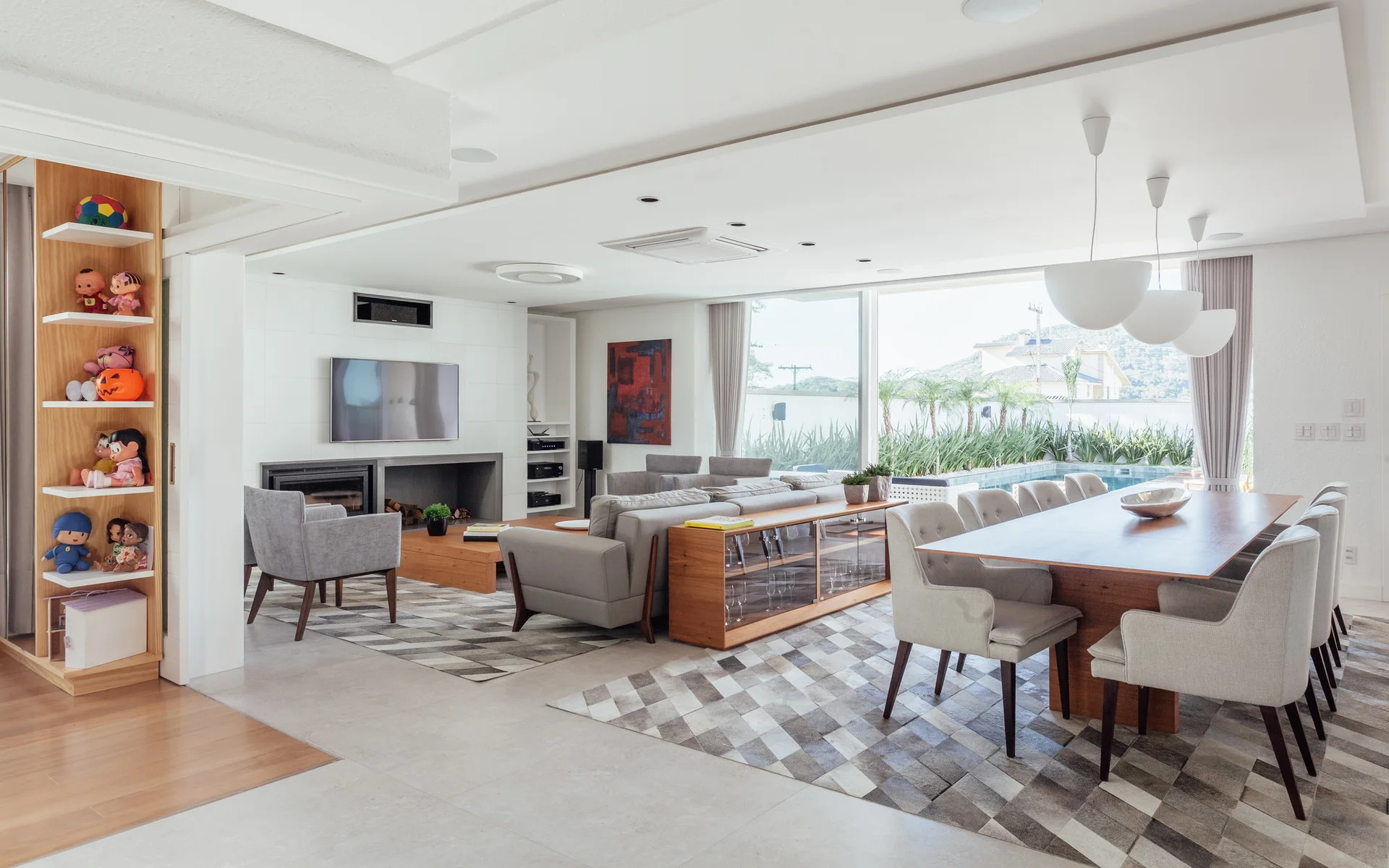 A bright open-concept living and dining room with grey sofas, a wooden dining table, and matching geometric rugs.